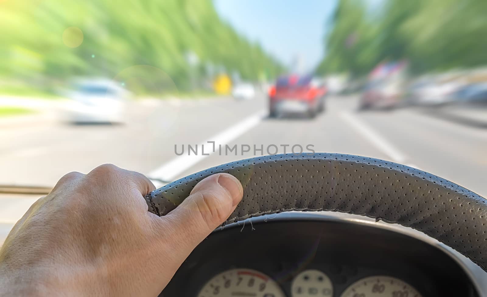 the driver hand on the steering wheel of a car that passes through a city street