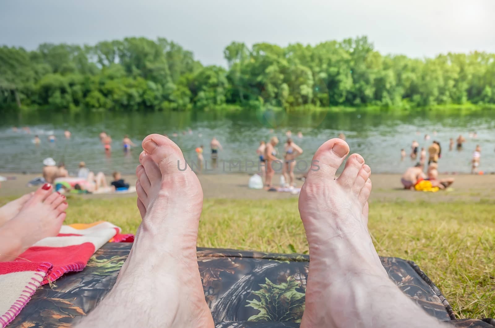 view of the legs of a lying person against the background of people swimming and relaxing on the beach