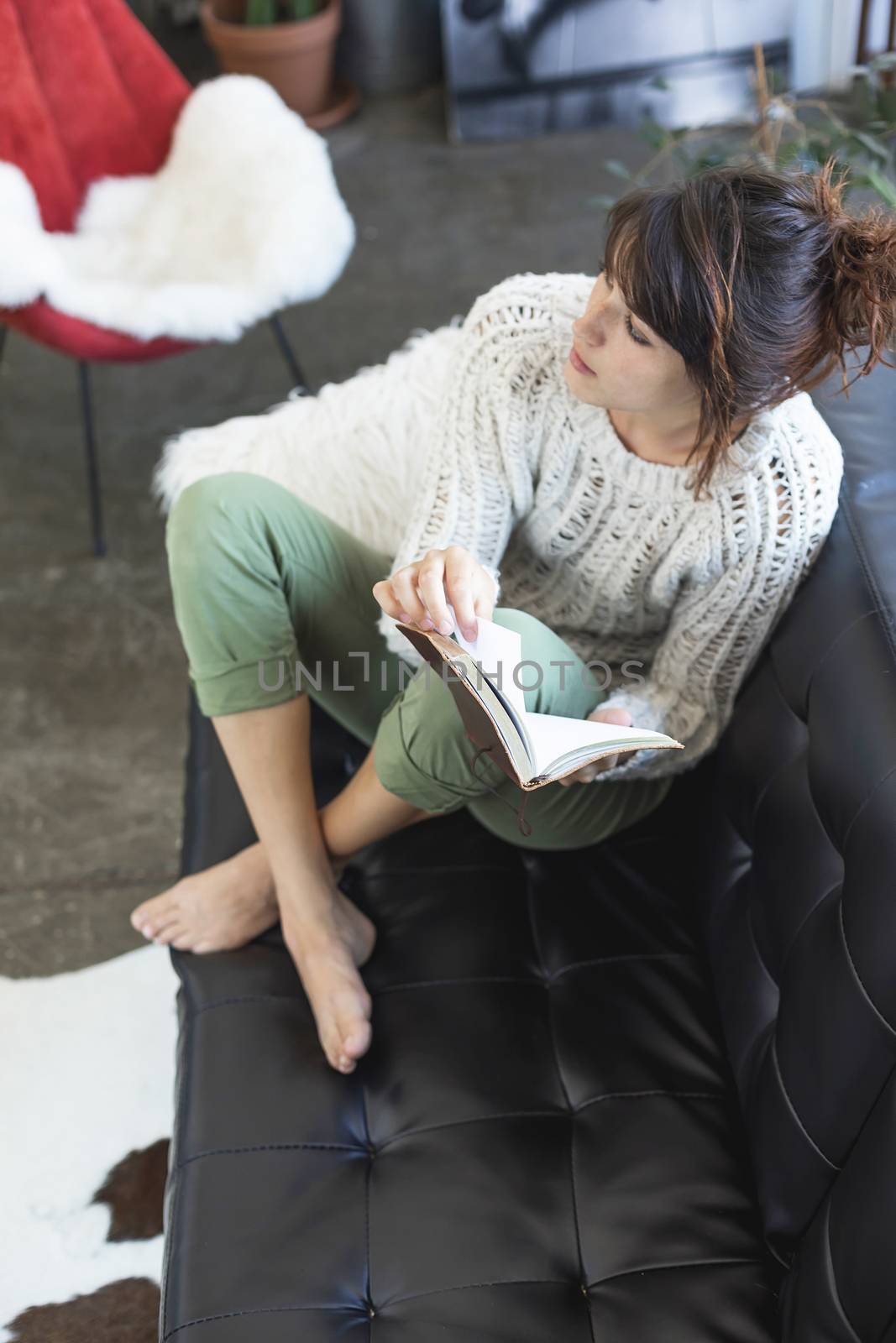 young pleased woman reading book while sitting on couch