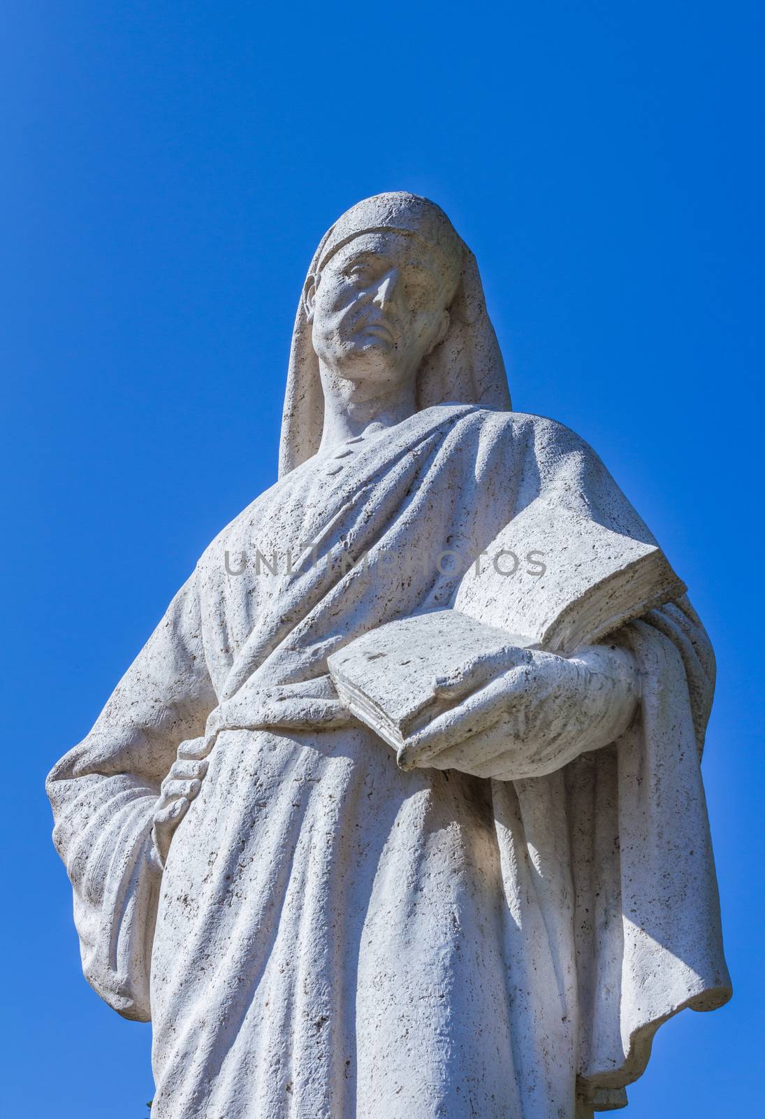 Statue of Poet Dante Alighieri with blue sky in the background. The writer has a book in his hand.