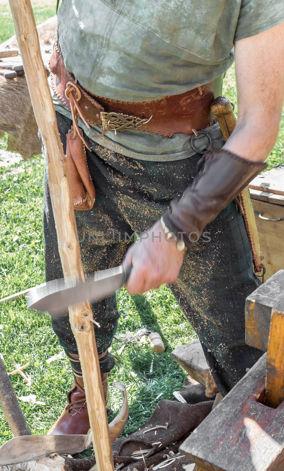 Craftsman with traditional medieval clothes manufactures a wooden arch with ancient method. Close up. Shallow deep of field.
