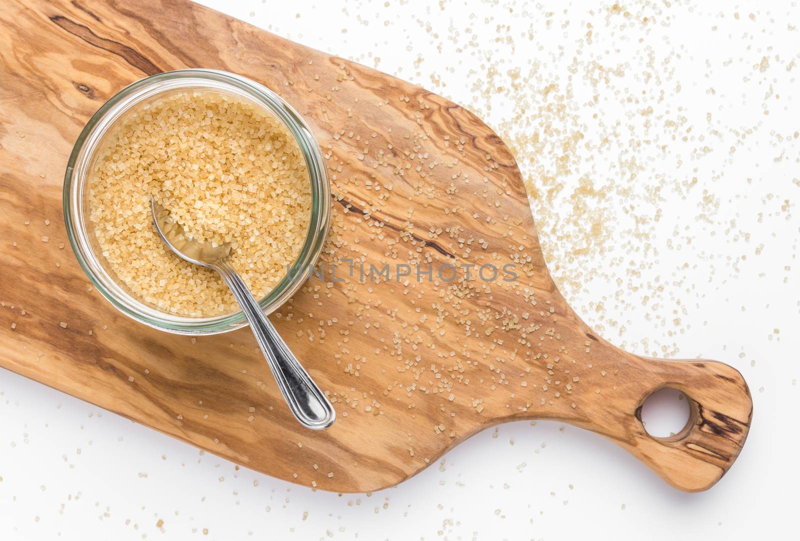 Organic brown sugar in glass jar on wooden chopping board. Top view.