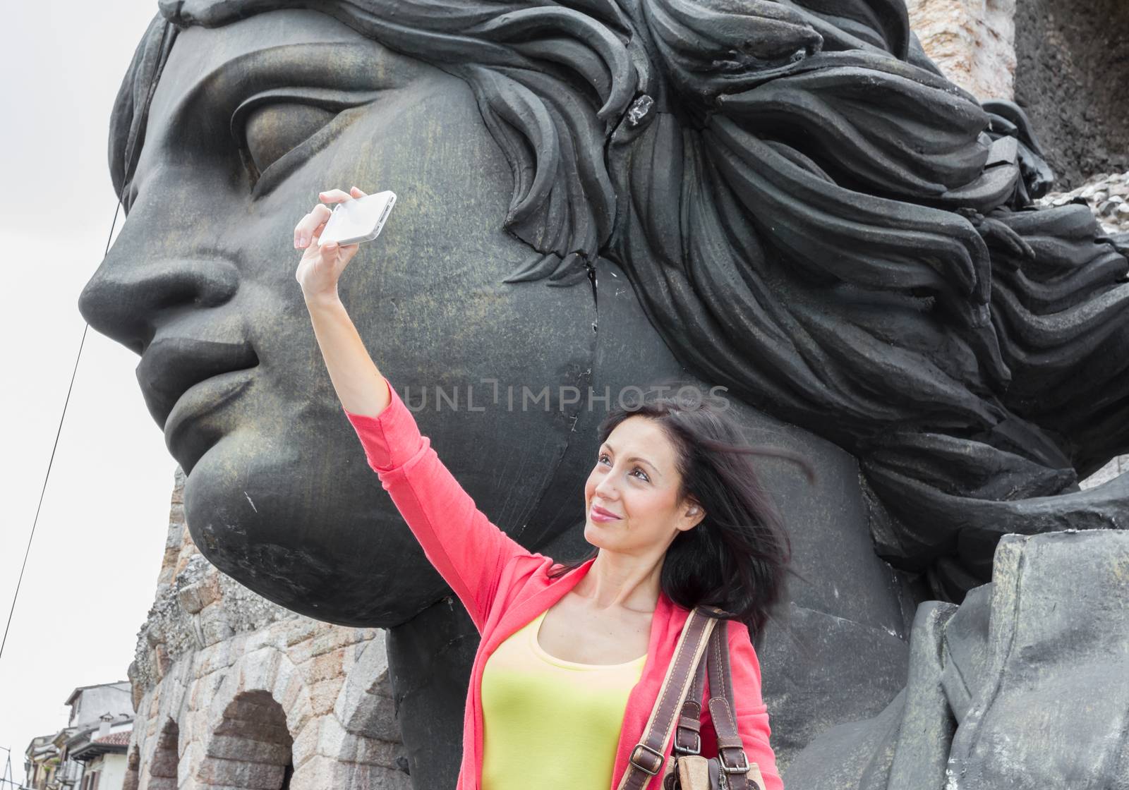 Young woman traveler making selfie photo with details of the Arena in Verona (Italy) and scenic decorations on background. Shallow DOF.