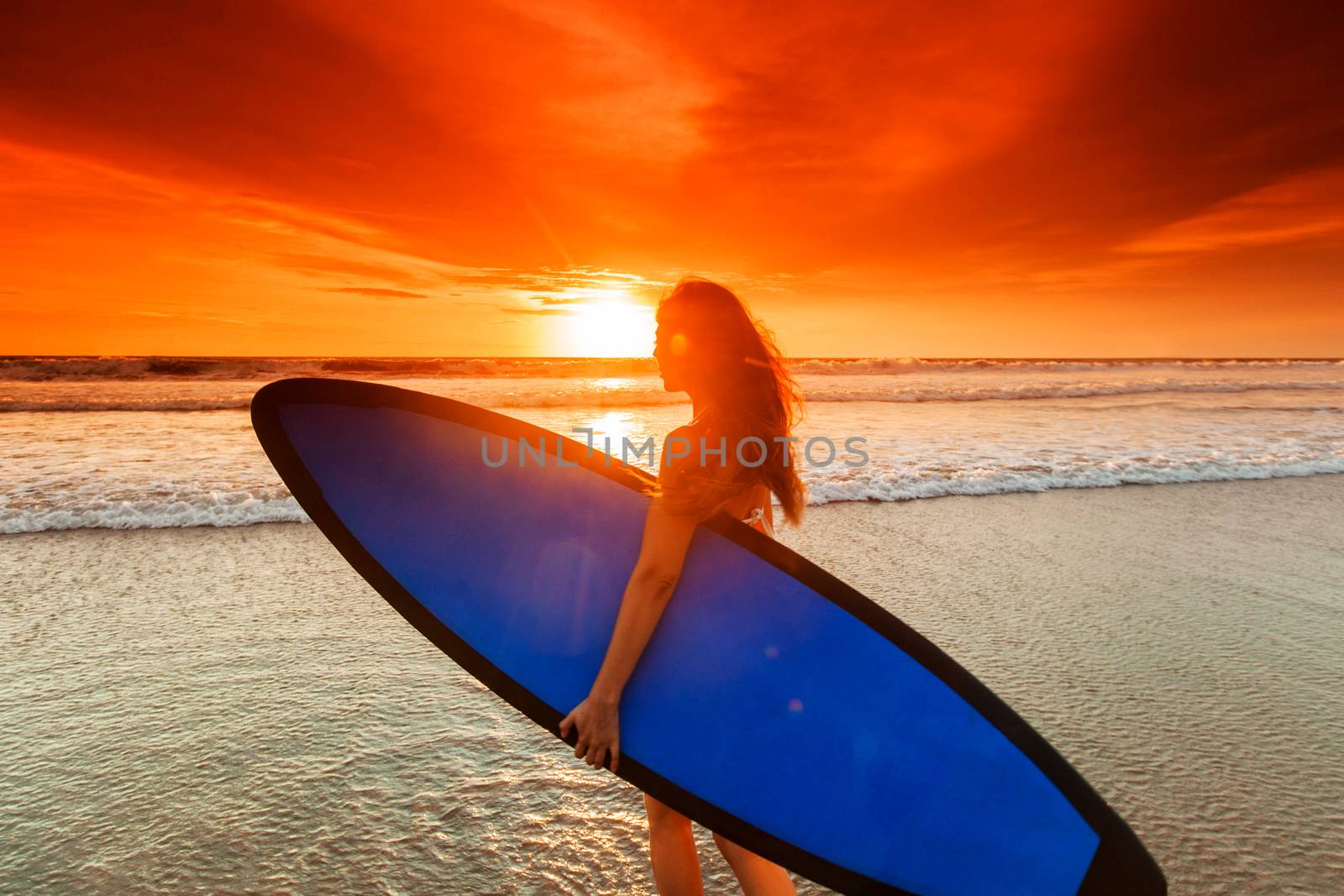 Beautiful mixed race woman on tropical beach holding surfboard at sunset