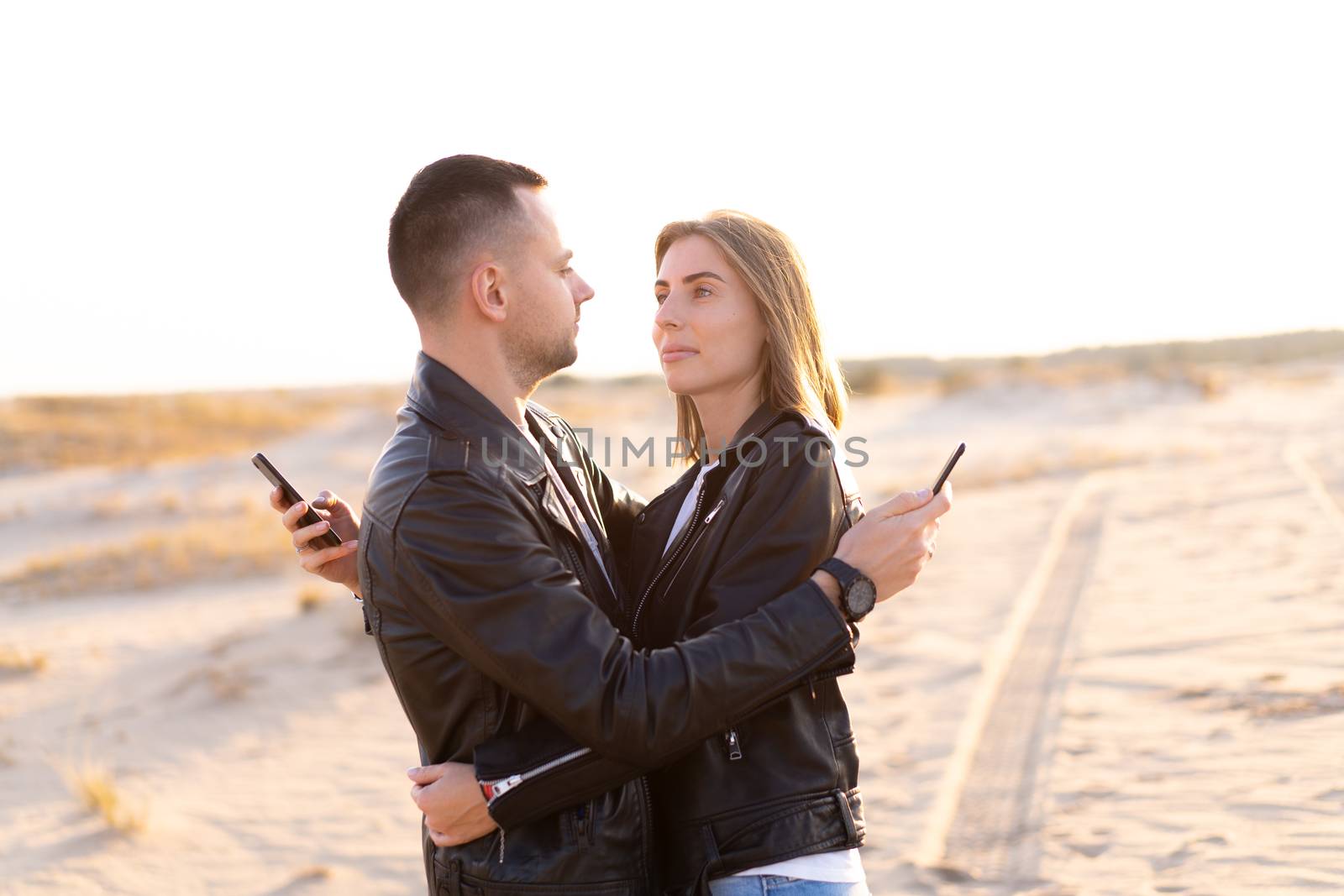 Happy and cute adorable adult couple leather jacket and jeans man with woman girlfriend walking Concept about how mobile phones social networks and the Internet affects the relationship between people