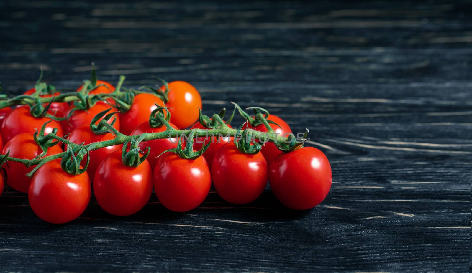 Cherry tomatoes on the dark black wooden table by andreonegin