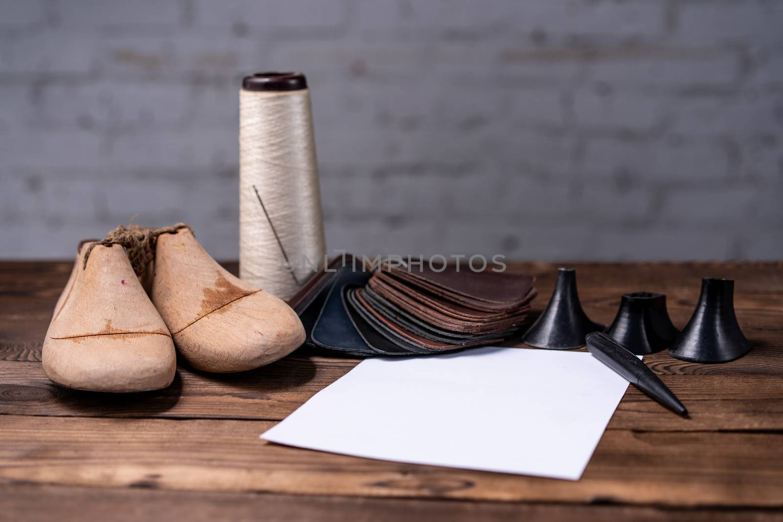 Leather samples for shoes and wooden shoe last on dark wooden table with Empty white sheet of paper for notes.. Designer furniture clothes. Shoe maker workspace.