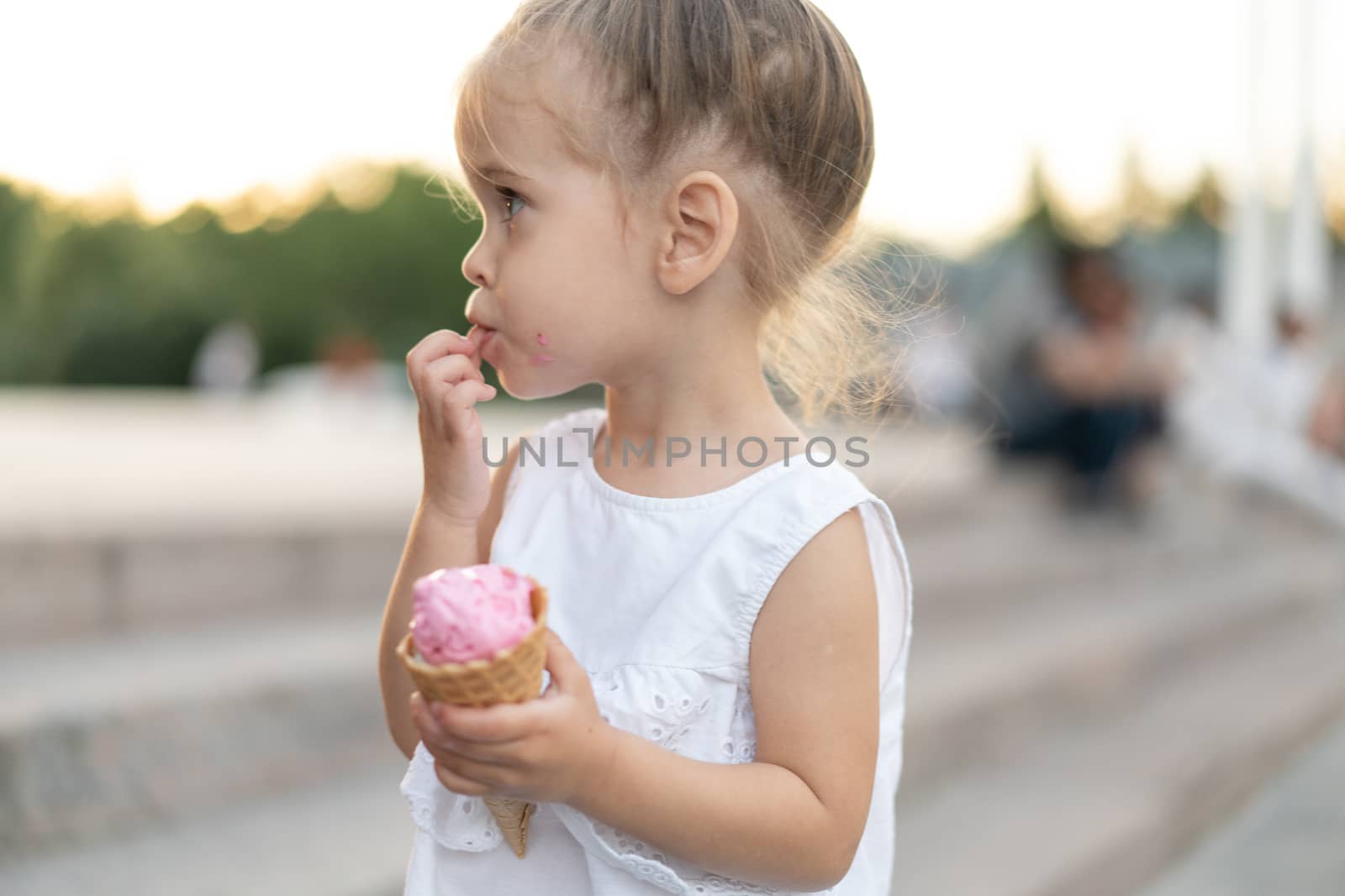 Little caucasian girl 3 years old eats ice cream closeup portrait. Summertime. Childhood Child with frozen dessert in hand walking outdoor. Close up portrait european girl witn ice-cream.
