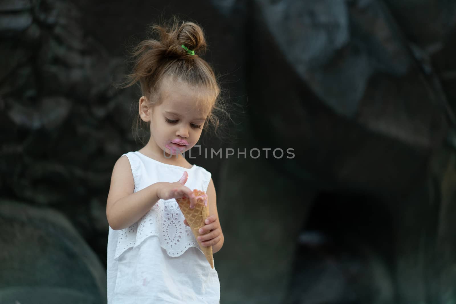 Little caucasian girl 3 years old eats ice cream closeup portrait. Summertime. Childhood Child with frozen dessert in hand walking outdoor. Close up portrait european girl witn ice-cream.