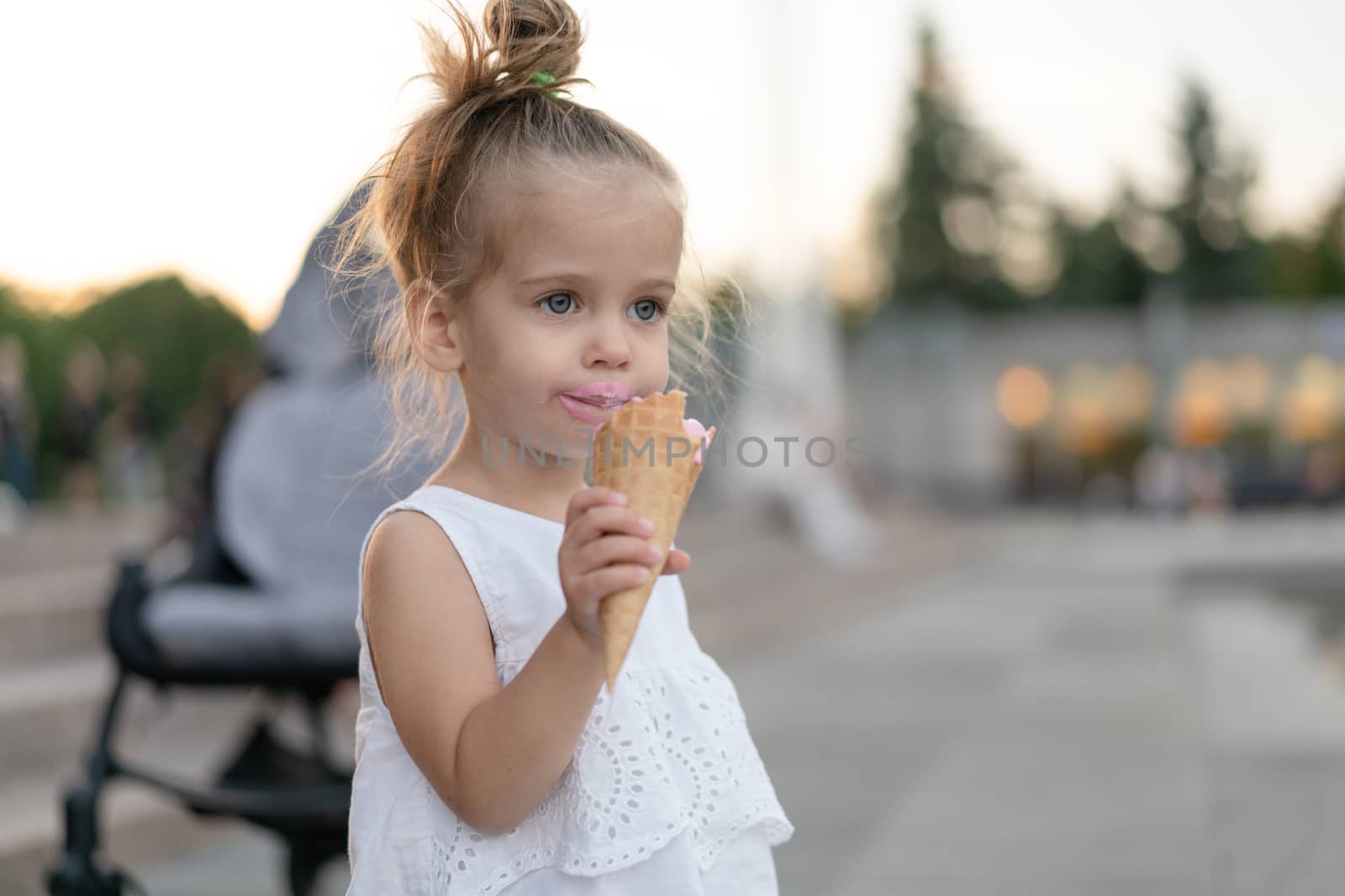 Little caucasian girl 3 years old eats ice cream closeup portrait. Summertime. Childhood Child with frozen dessert in hand walking outdoor. Close up portrait european girl witn ice-cream.