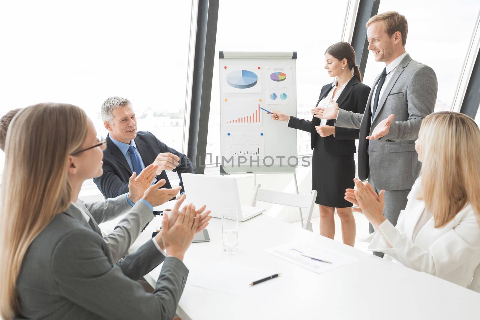 Business people giving presentation using financial diagrams at flipchart to colleagues in office at meeting