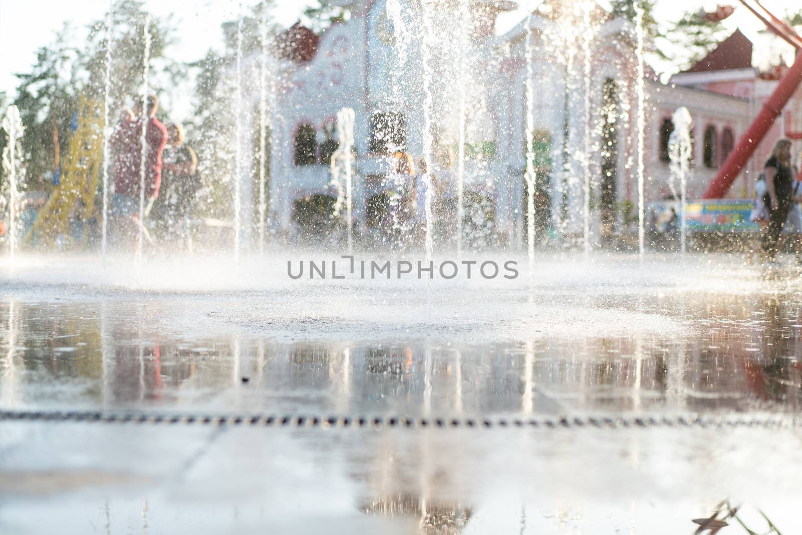 Unrecognizable Happy kids have fun playing in city dry water fountain on hot summer day. Parents with their children. Active family leisure. Summertime concept