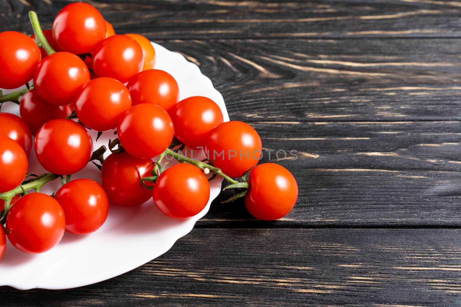 Cherry tomatoes in the white plate on the wooden table by andreonegin