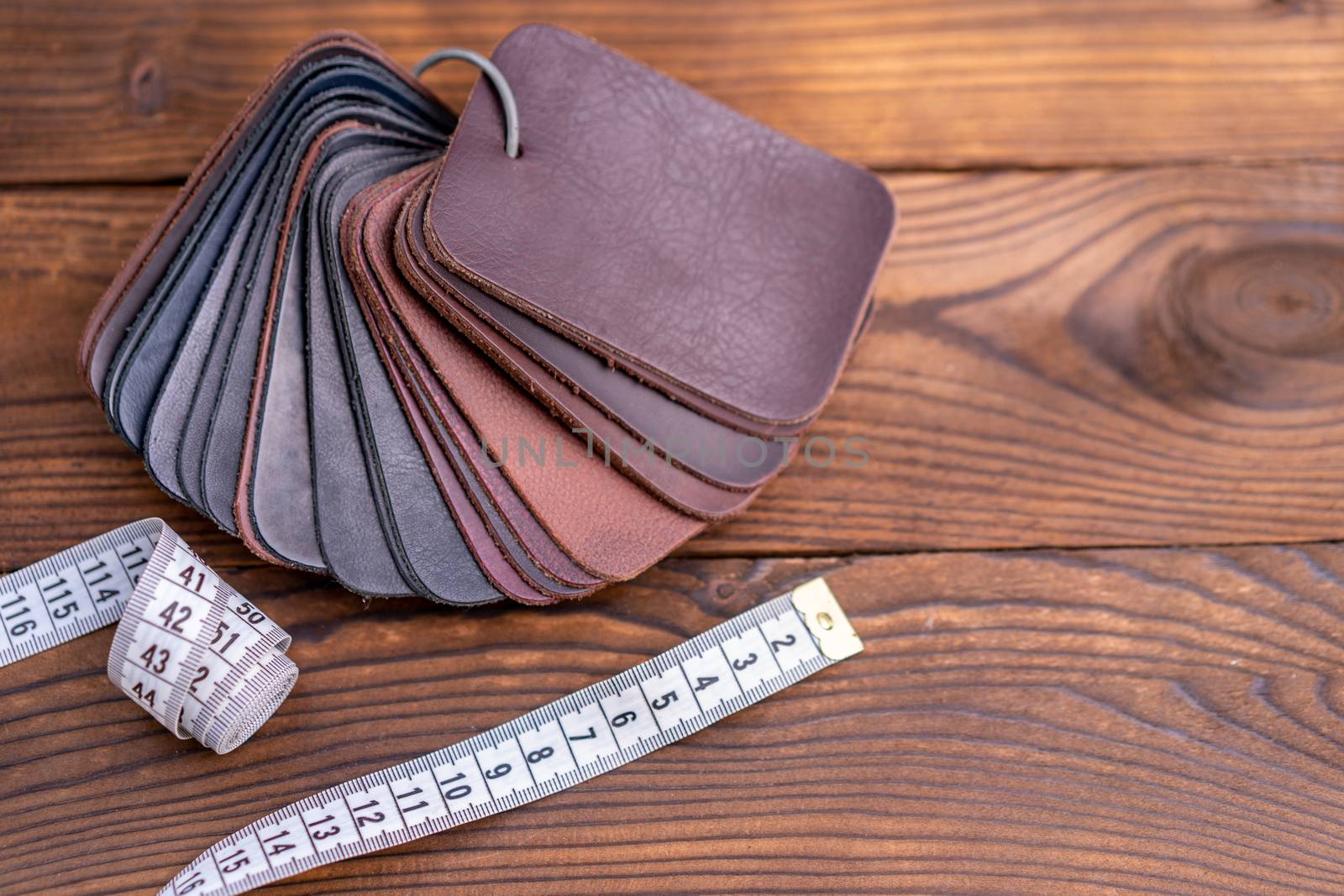 Leather samples for shoes and measuring tape on dark wooden table. Designer furniture clothes.