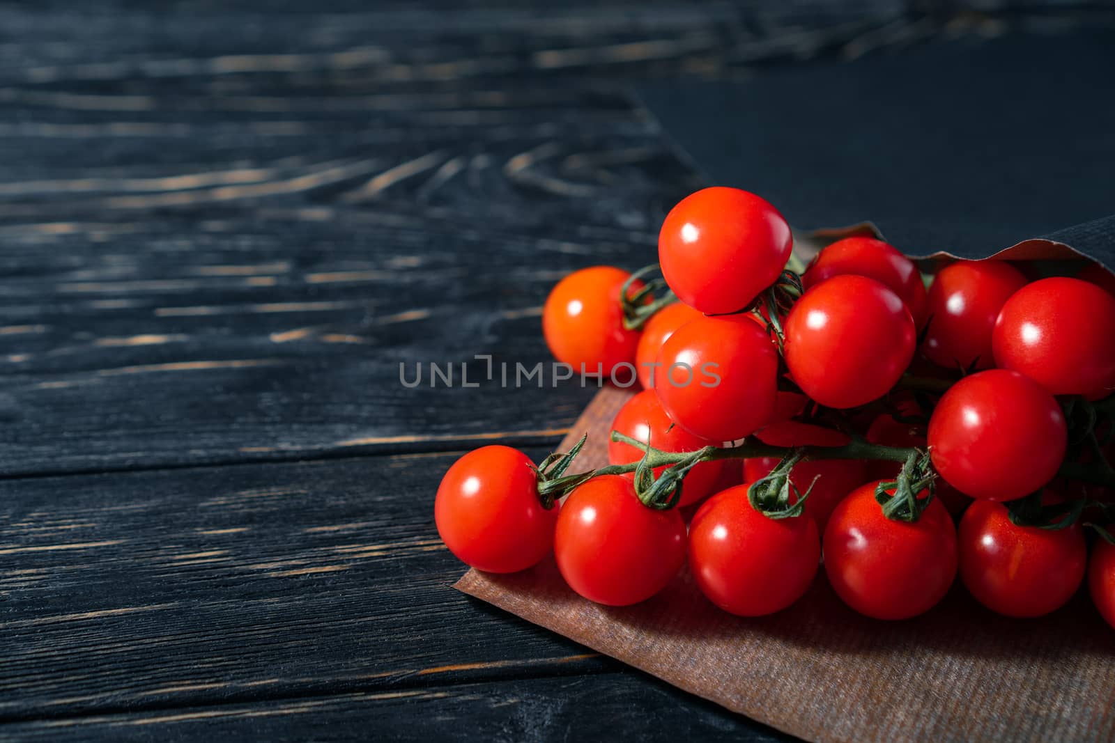 Cherry tomatoes in the paper packaging on the wooden table by andreonegin