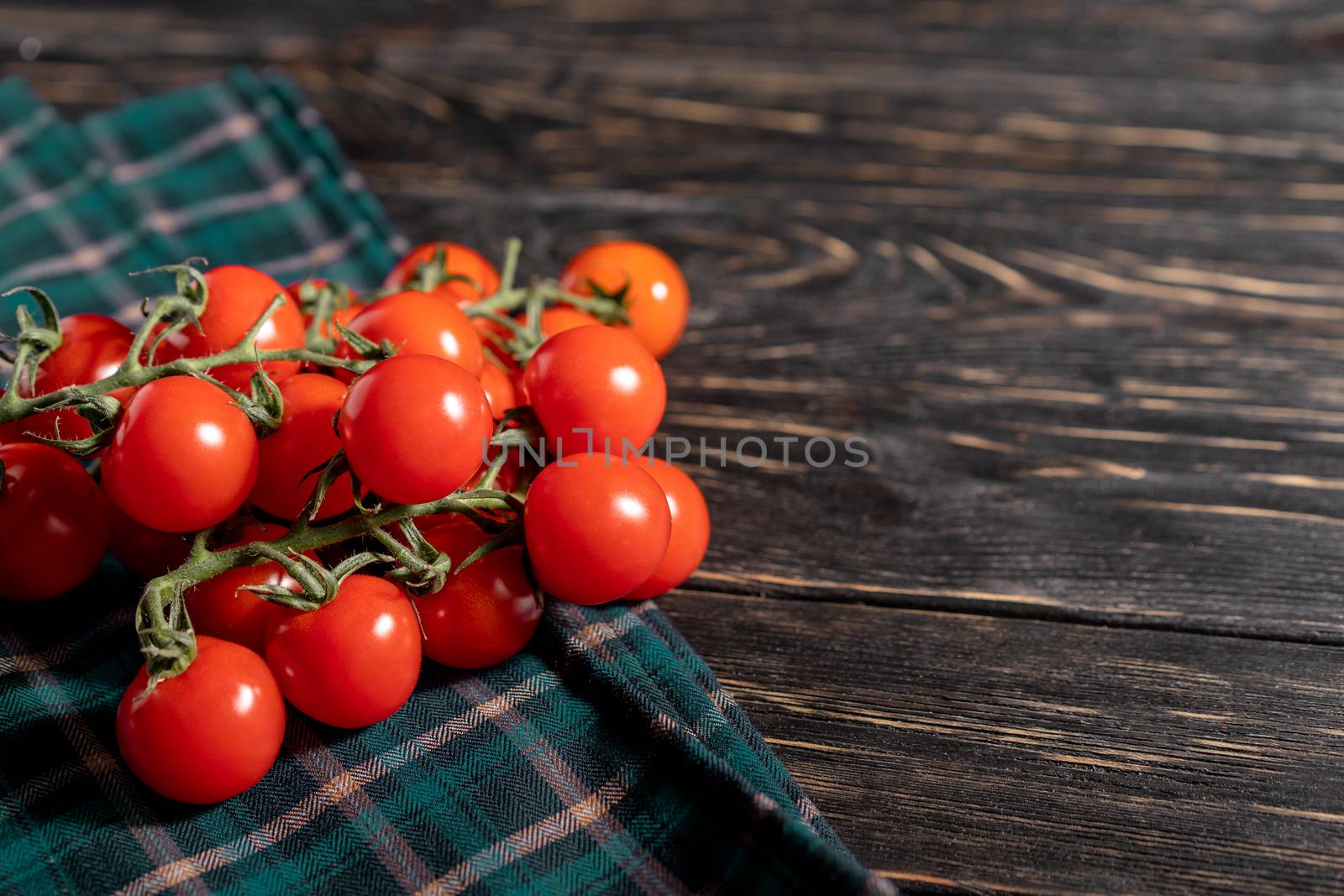 Cherry tomatoes in the checkered cloth serviette on the wooden table by andreonegin