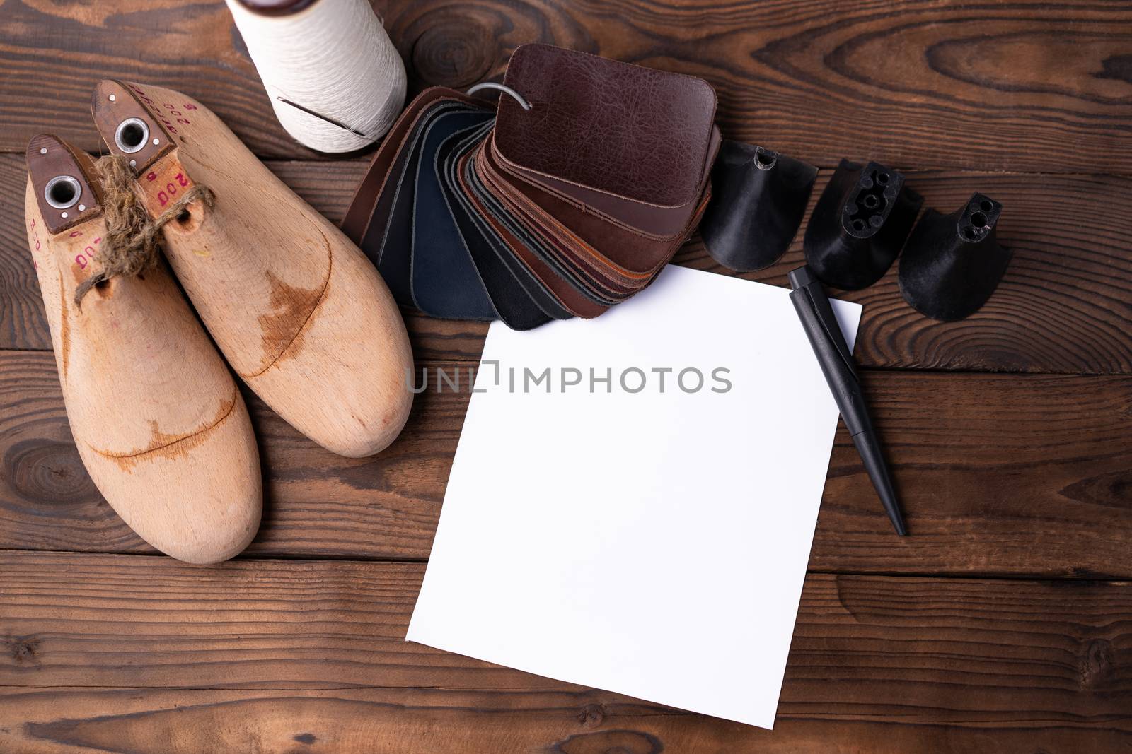 Leather samples for shoes and wooden shoe last on dark wooden table with Empty white sheet of paper for notes.. Designer furniture clothes. Shoe maker workspace.