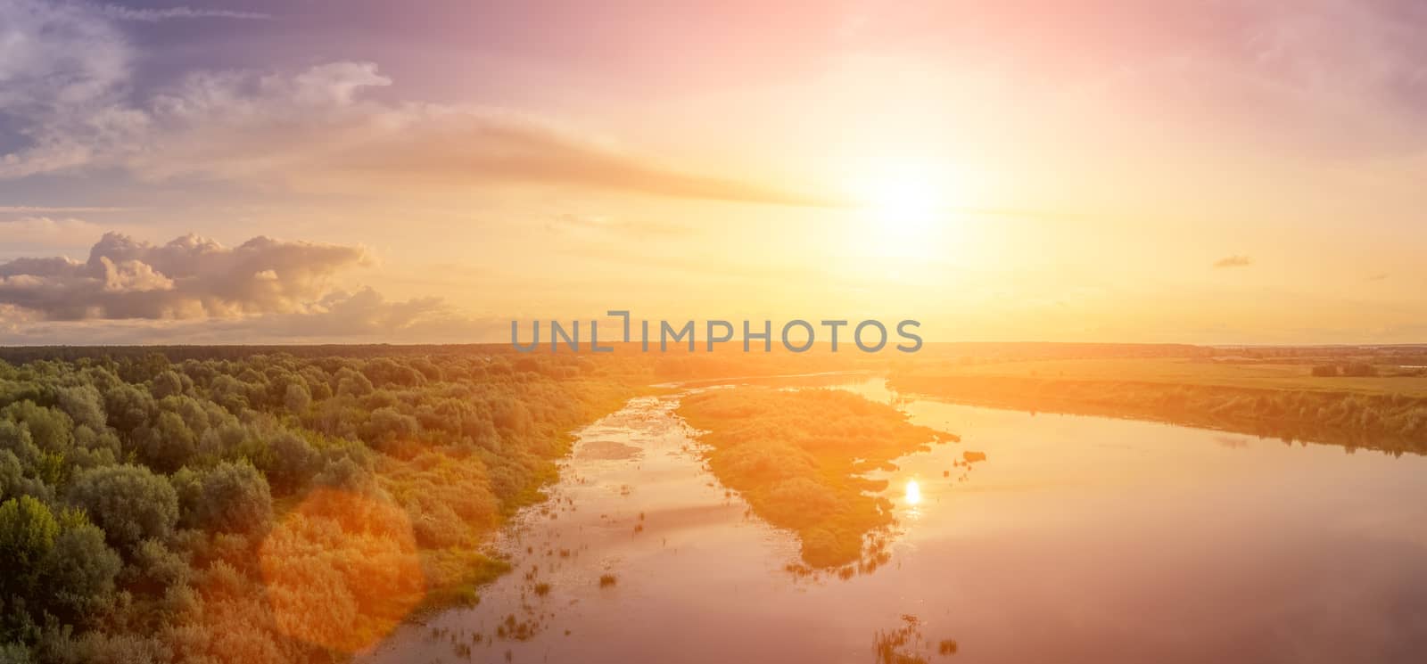 Aerial view to sunset on the river at summer evening with clouds and trees. Water reflection of a sky.