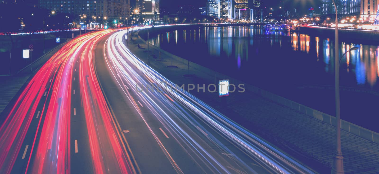 Moving car with blur light through city at night near Moscow river embankment and illuminated Radisson or Ukraine hotel. Moscow, Russia.