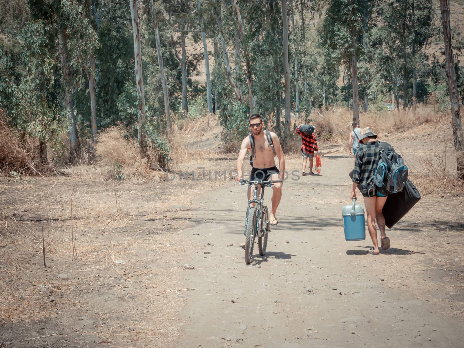 Jordan Valley, Israel - May 28, 2020: Many hikers walking or riding a bike on a dirt road on a sunny summer day. They carry staff for camping near the Jordan River. Adventure vacation.