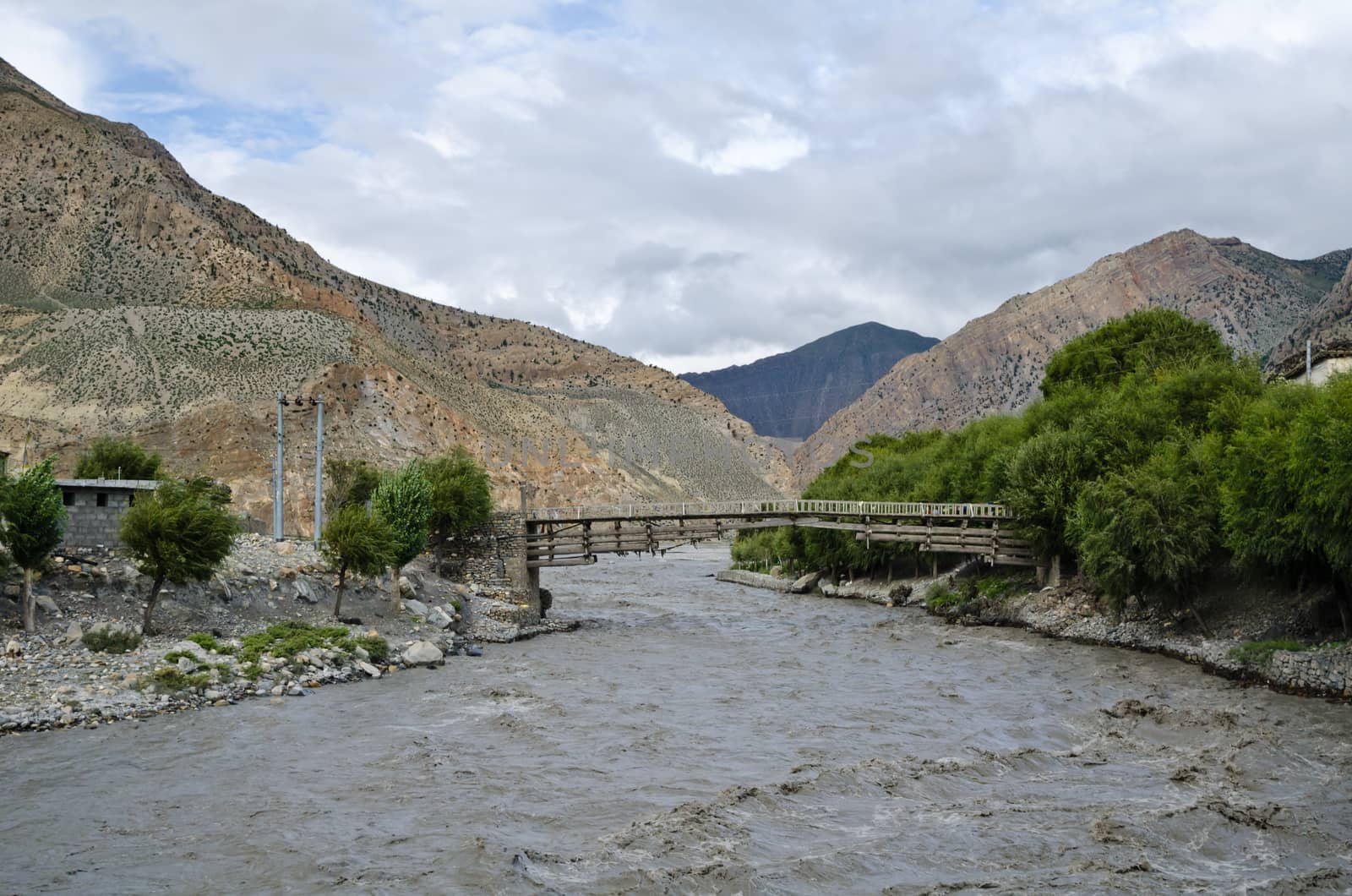 The bridge across fast, affluent and muddy mountain Nepal river near Jomsom village