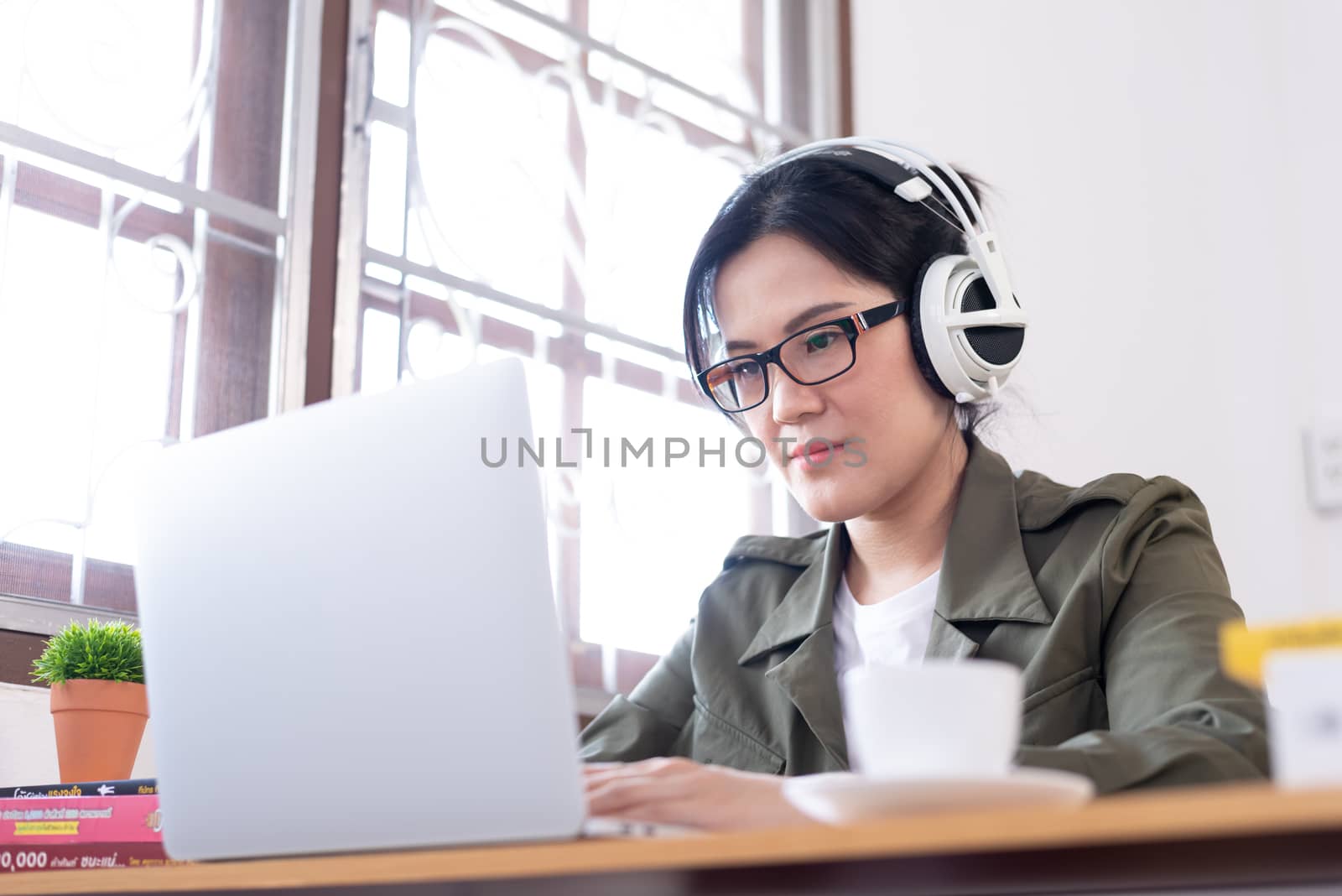 Modern young Asian woman working from home and listening to the music with a white headphones.