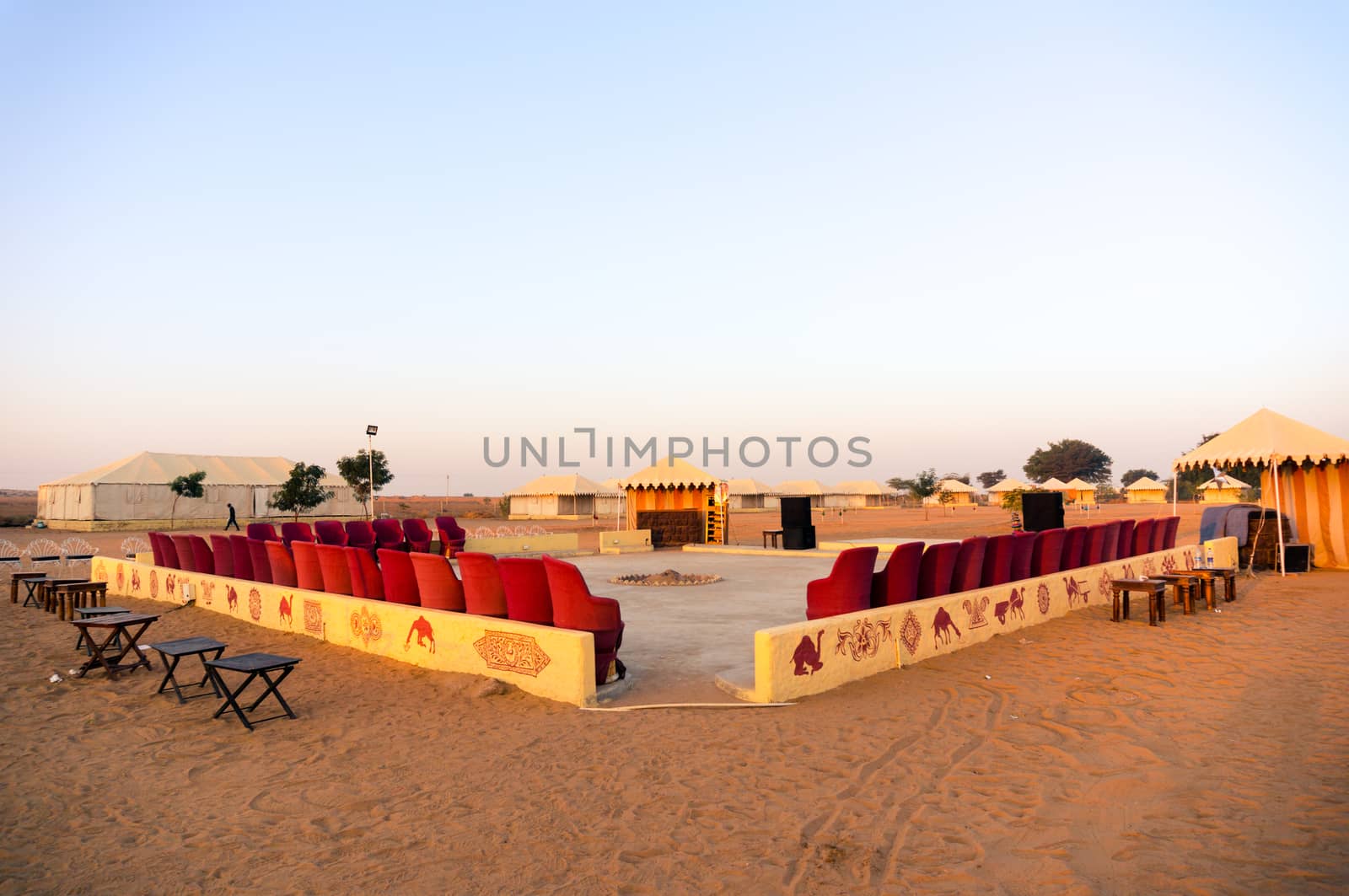 Wide angle shot of seating and entertainment area of a desert camp with sand around and tents in the distance. Shows the entertainment area in these adventure camps made for tourists and travellers