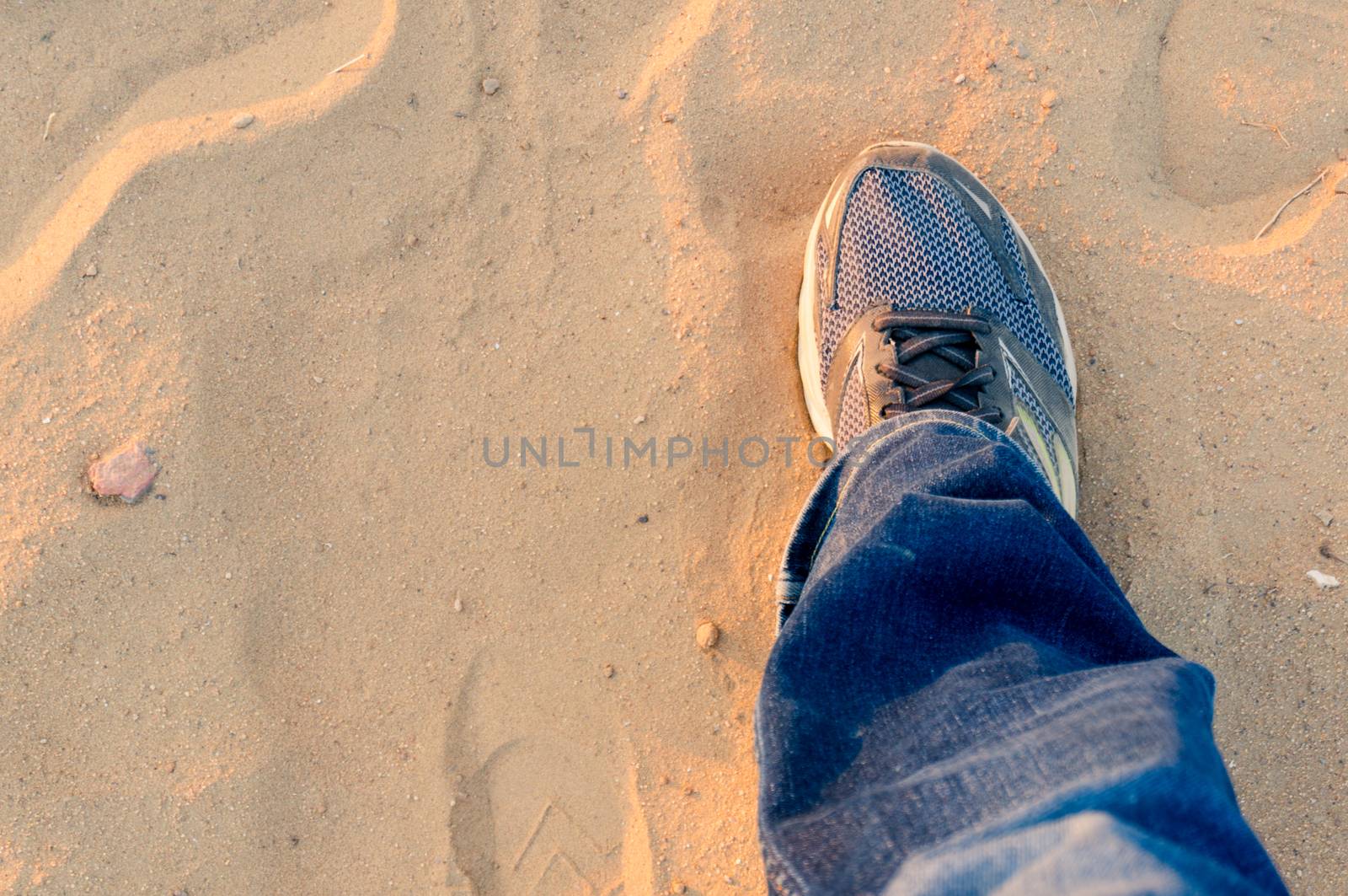 Top down view of man extending a foot with a worn sneaker jeans on dusty sand showing travel and trekking during evening as sunlight bounces off it. Shows wanderlust and travel in India which has been stopped by the lockdown and the epidemic