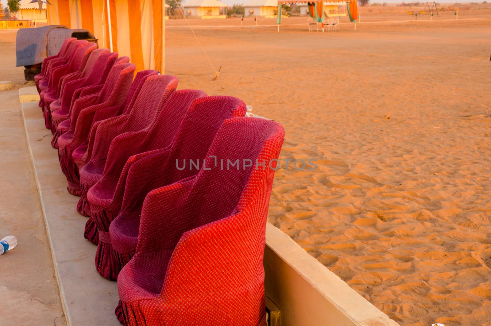 Close up shot of red muddha cane chairs sofas with small yellow brick walls for seating visitors during a performance with desert sand in the background. Shot in the evening it shows the hours just before the traditional dances and performances start