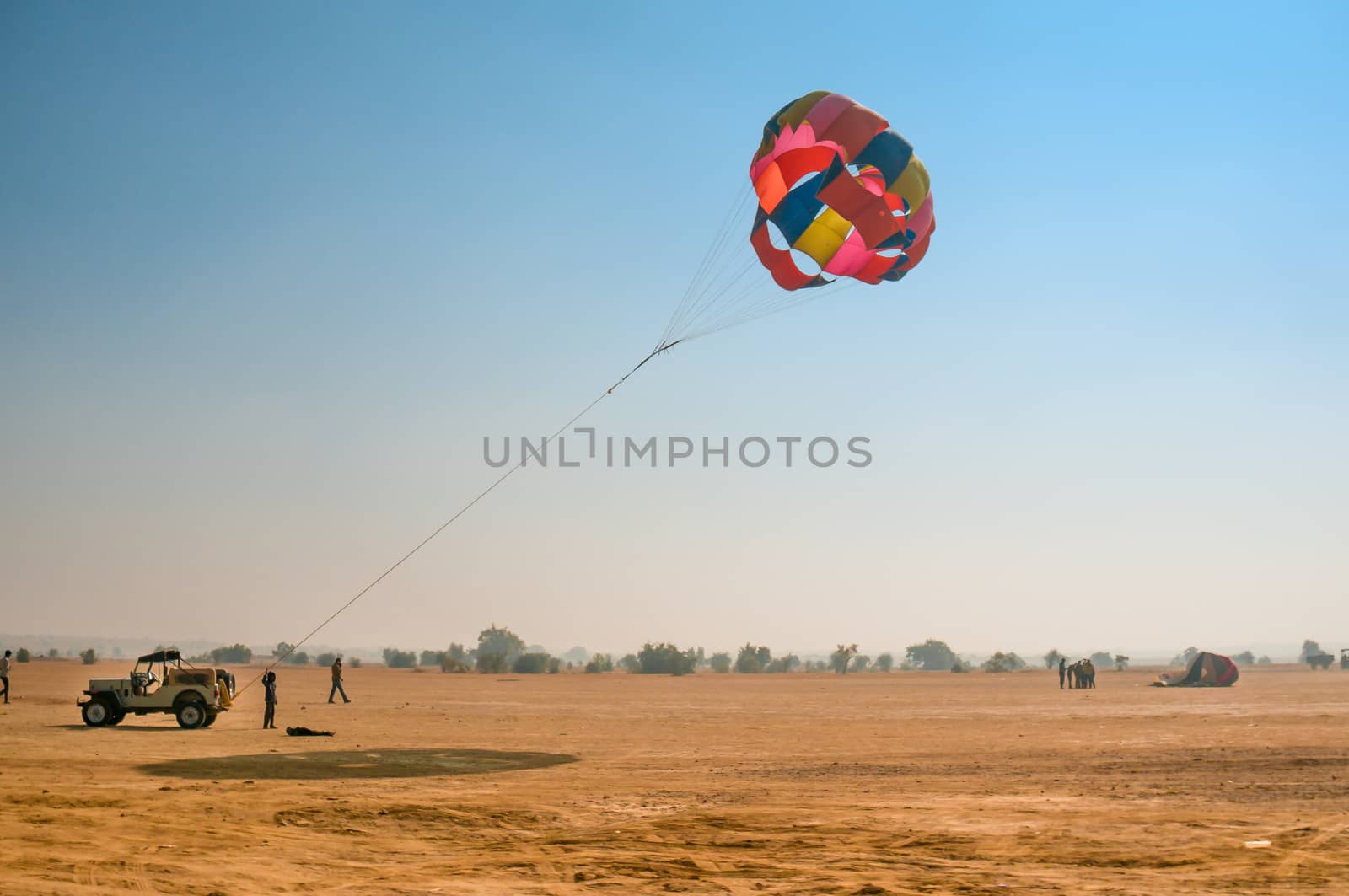 Jeep towing a parachute for adventure para gliding in the empty barren thar desert in rajasthan near jaisalmer and sum. Shows the various adventure sport options available on road trips in this state