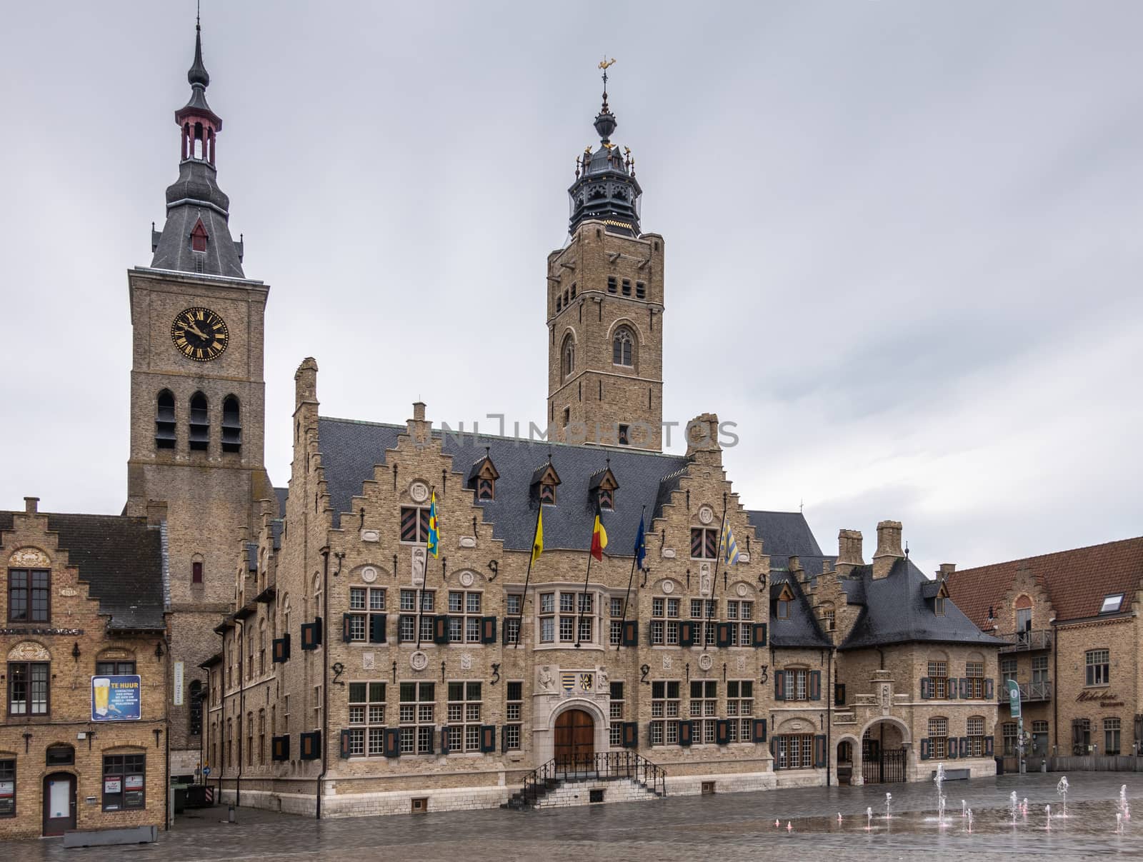 Diksmuide, Flanders, Belgium -  June 19, 2019: Grote Markt. Brown brick historic City Hall, or Stadhuis, building under light blue sky. Rain Wet market square. Saint Nicolas church clock tower in back.