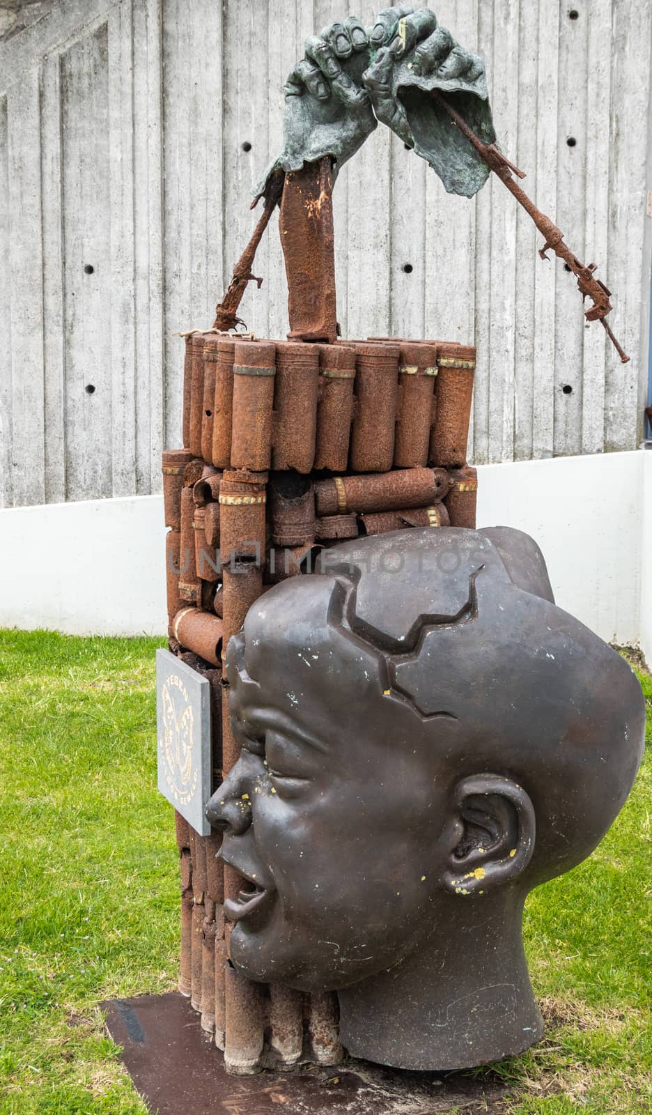 Diksmuide, Flanders, Belgium -  June 19, 2019: Old war-iron monument at IJzertoren, tallest peace monument of WW 1. Rusty bomb shells, crying baby head, hands against gray wall.
