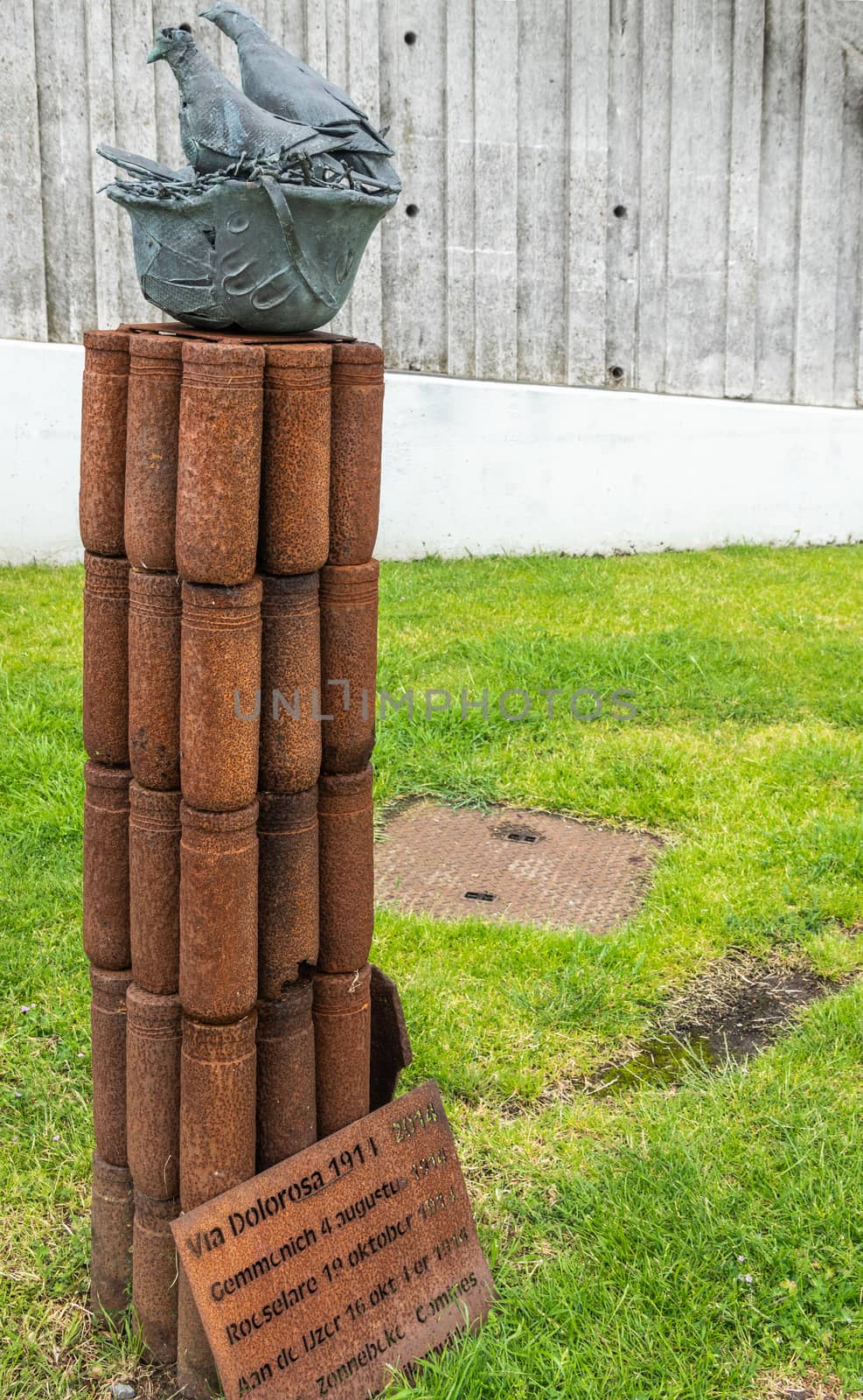 Diksmuide, Flanders, Belgium -  June 19, 2019: Old war-iron monument at IJzertoren, tallest peace monument of WW 1. Rusty bomb shells, pigeons in helmets, against gray wall, green lawn.
