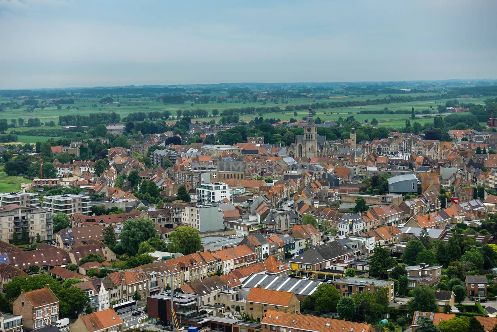 Diksmuide, Flanders, Belgium -  June 19, 2019: View on dowtown from up IJzertoren, tallest peace monument of WW 1. Brick buildings with red roofs, towers of church and city hall, green pasture.