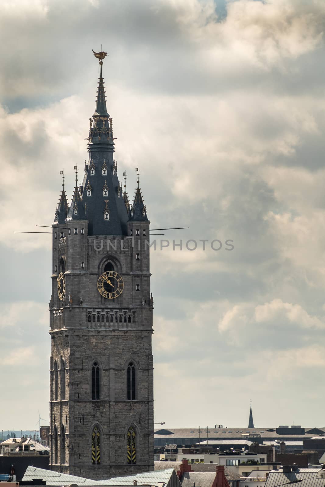 Gent, Flanders, Belgium -  June 21, 2019: Shot from castle tower, view over city roofs shows closeup of Belfry Tower against heavy white cloudscape with few blue patches.