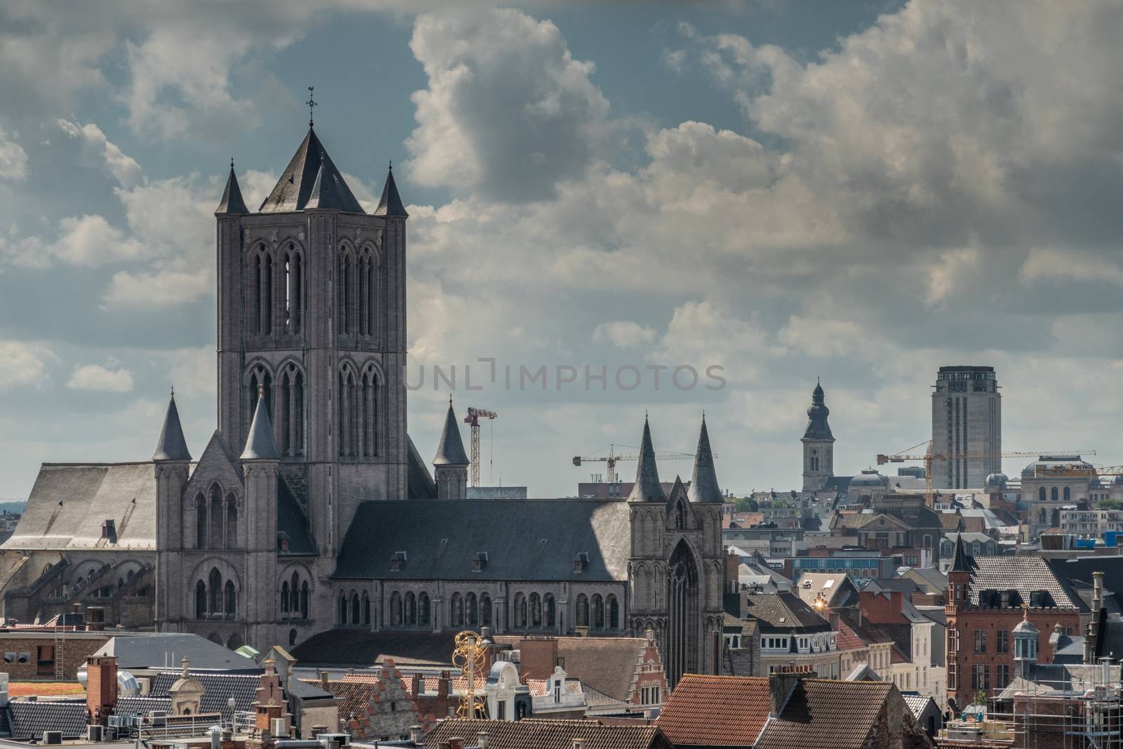 Gent, Flanders, Belgium -  June 21, 2019: Shot from castle tower, view over city roofs shows Sint Niklaas church with in back towers of University and Onze-Lieve-Vrouw-Sint-Pieters church under heavy cloudscape.