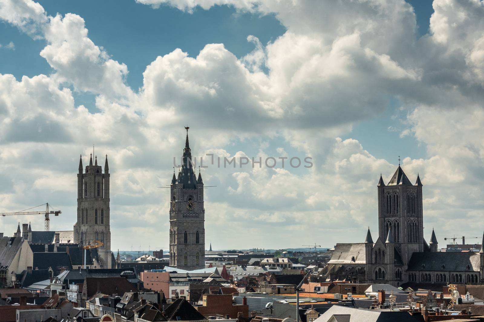 Gent, Flanders, Belgium -  June 21, 2019: Shot from castle tower, view over city roofs shows three most important and historic towers of Belfry, Cathedral and Sint Niklaas church under heavy cloudscape with blue patches.