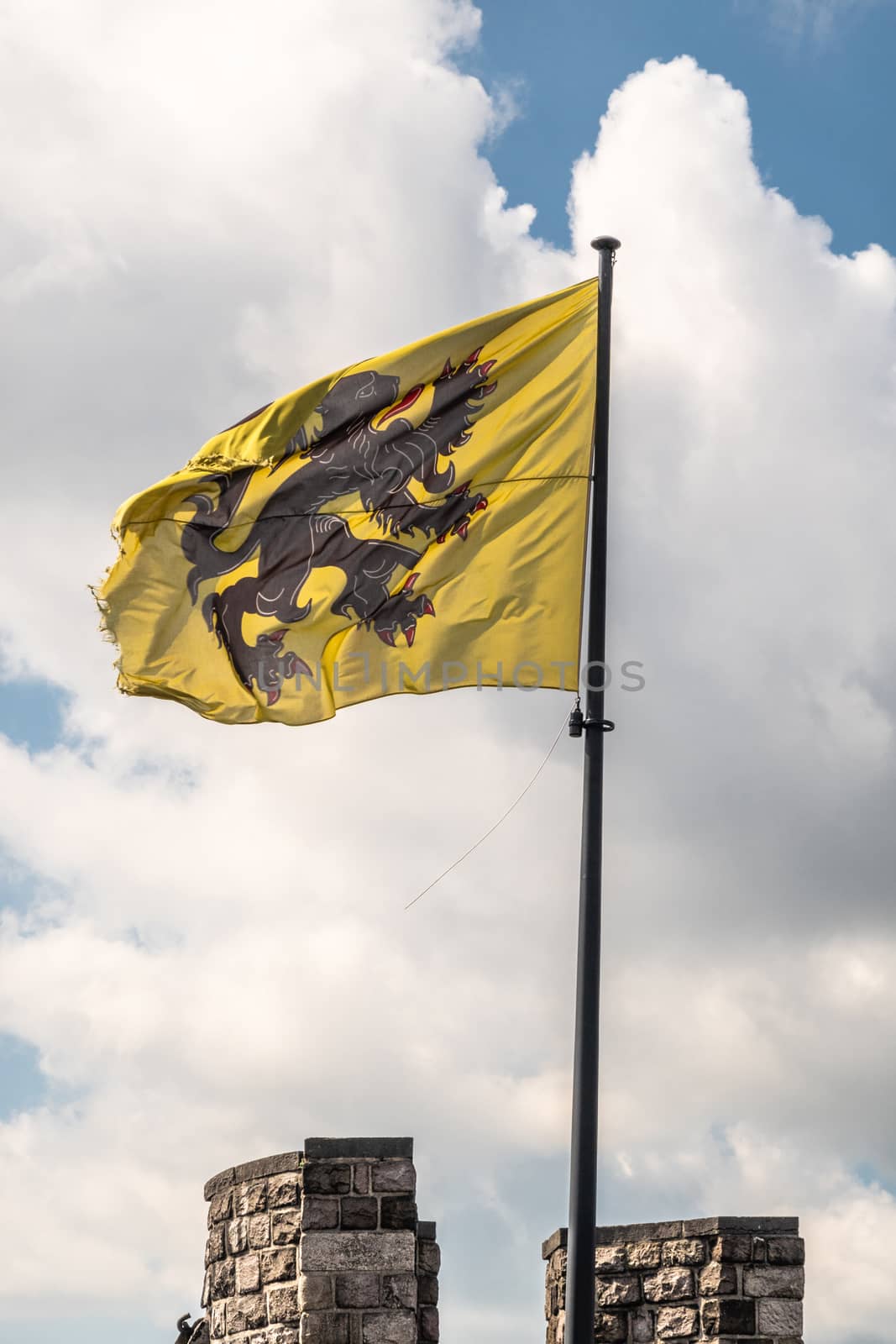 Gent, Flanders, Belgium -  June 21, 2019: Closeup of black-yellow-red flag of Flanders State on top of castle tower against white cloudscape with blue patches.