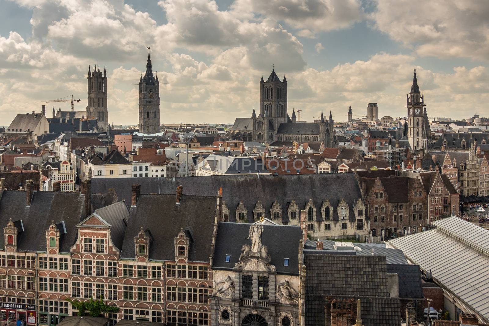 Gent, Flanders, Belgium -  June 21, 2019: Shot from castle tower, view over city roofs shows six most important and historic towers of Belfry, churches, Postal service, and university. Fish market gate. Cloudscape with blue patches.