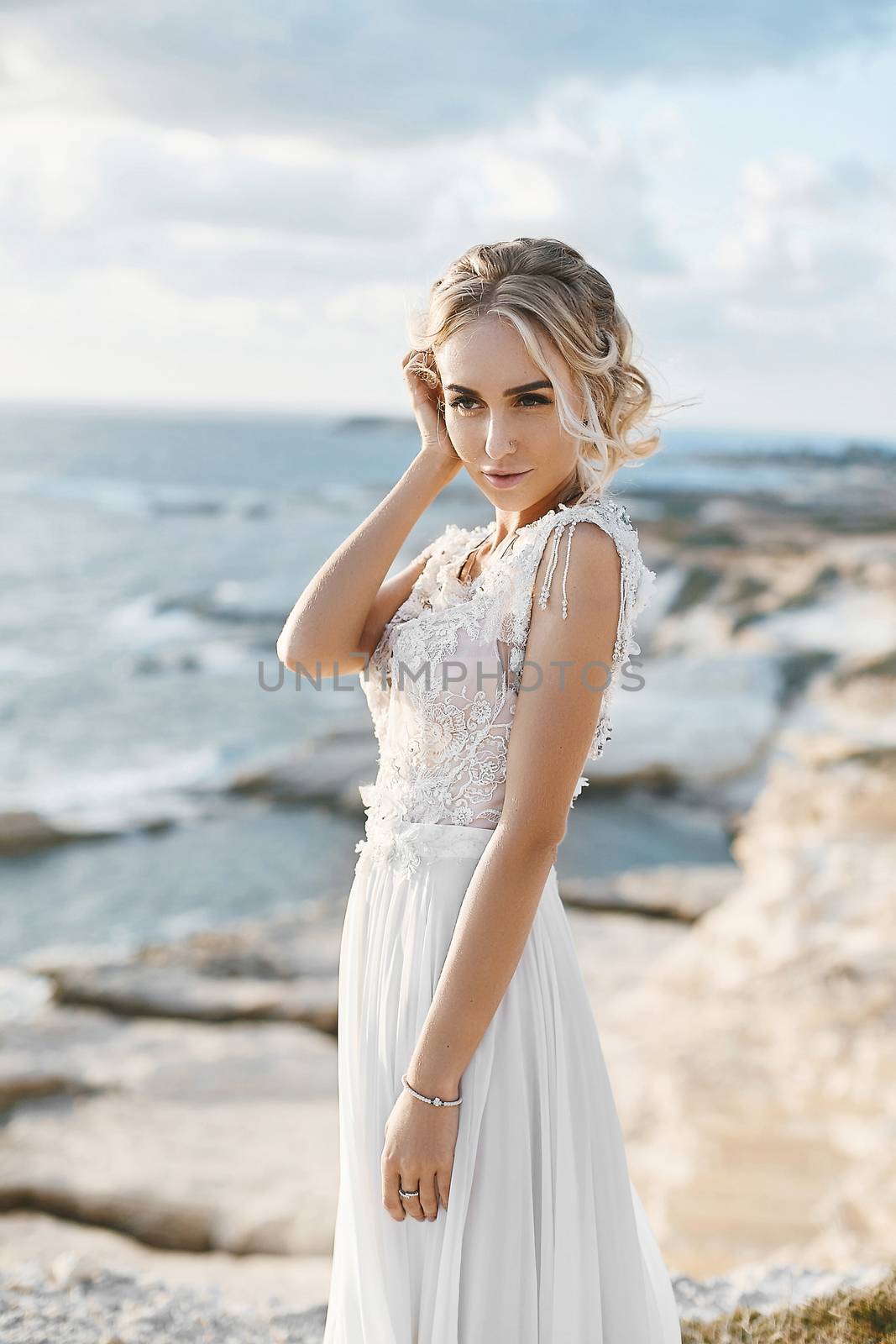 Beautiful young blonde model woman with nude makeup in a fashionable wedding dress walking at the sea coast at Cyprus.