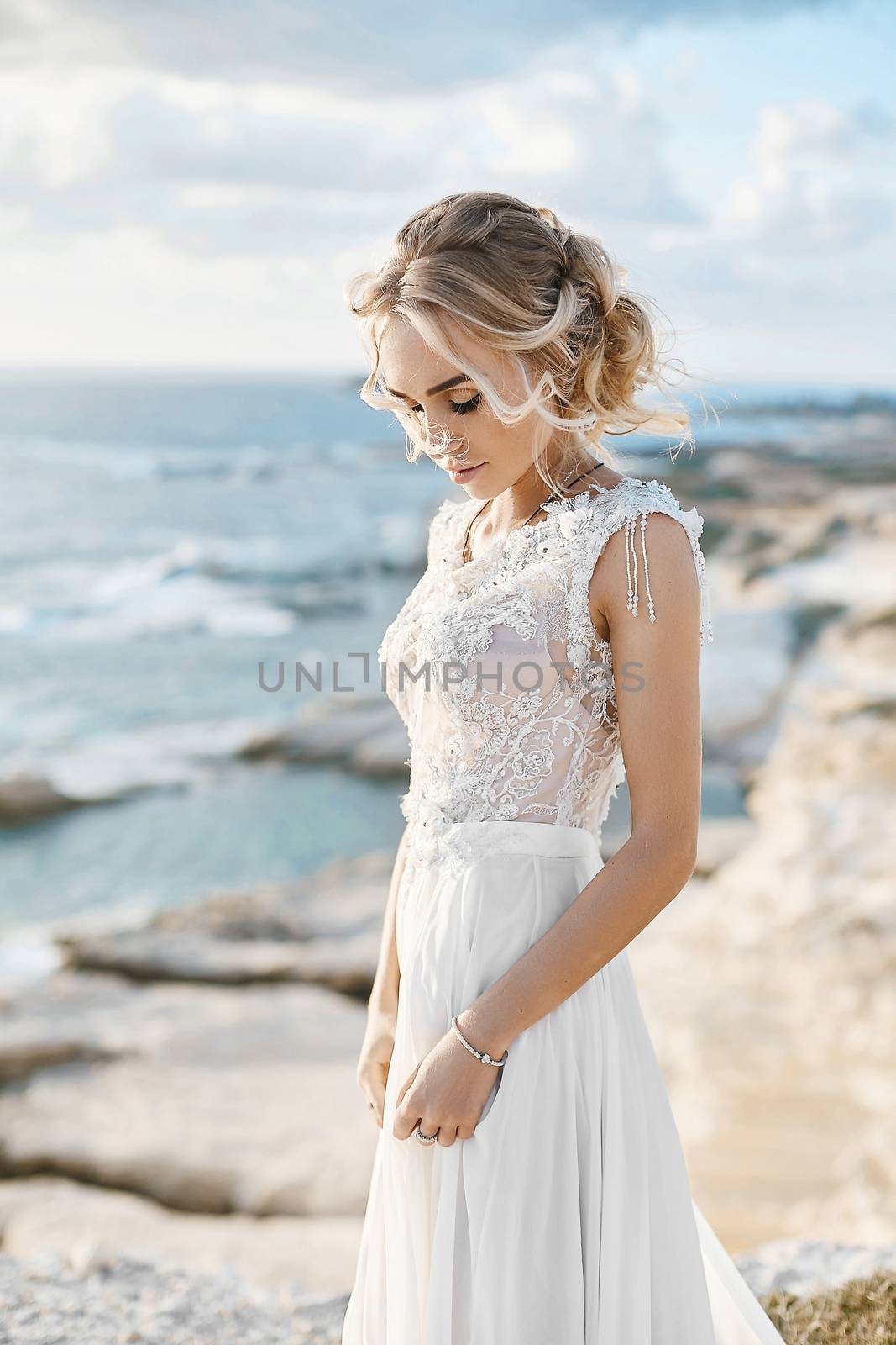 Beautiful young blonde model woman with nude makeup in a fashionable wedding dress walking at the sea coast at Cyprus.