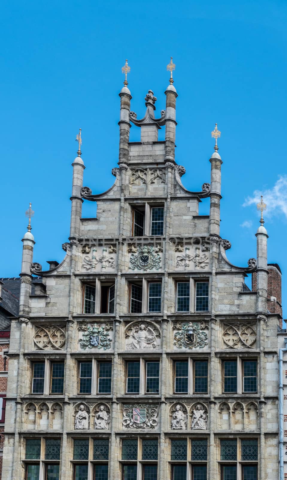 Gent, Flanders, Belgium -  June 21, 2019: Closeup of historic gray-stone gable of Graslei 8 building against blue sky. Frescoes on facade. Ornaments on top.