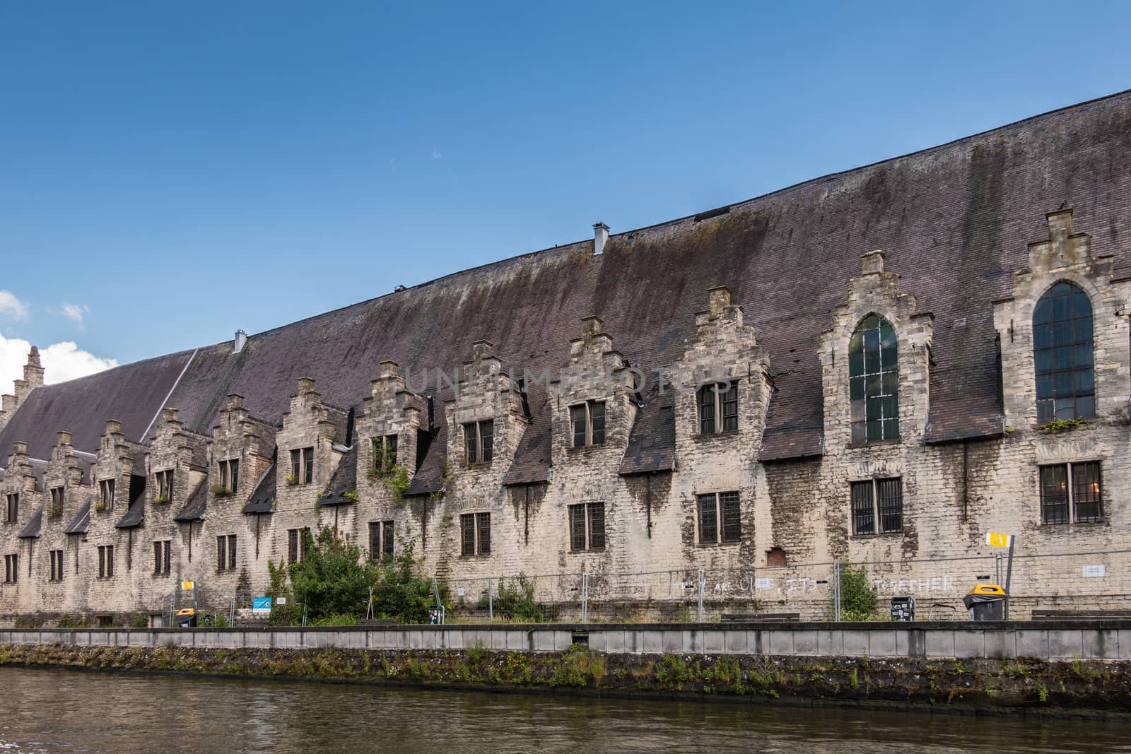 Gent, Flanders, Belgium -  June 21, 2019: Closeup of historic gray-stone long facade of Vleeshuis, medieval meat trading floor, along Leie River under blue sky.