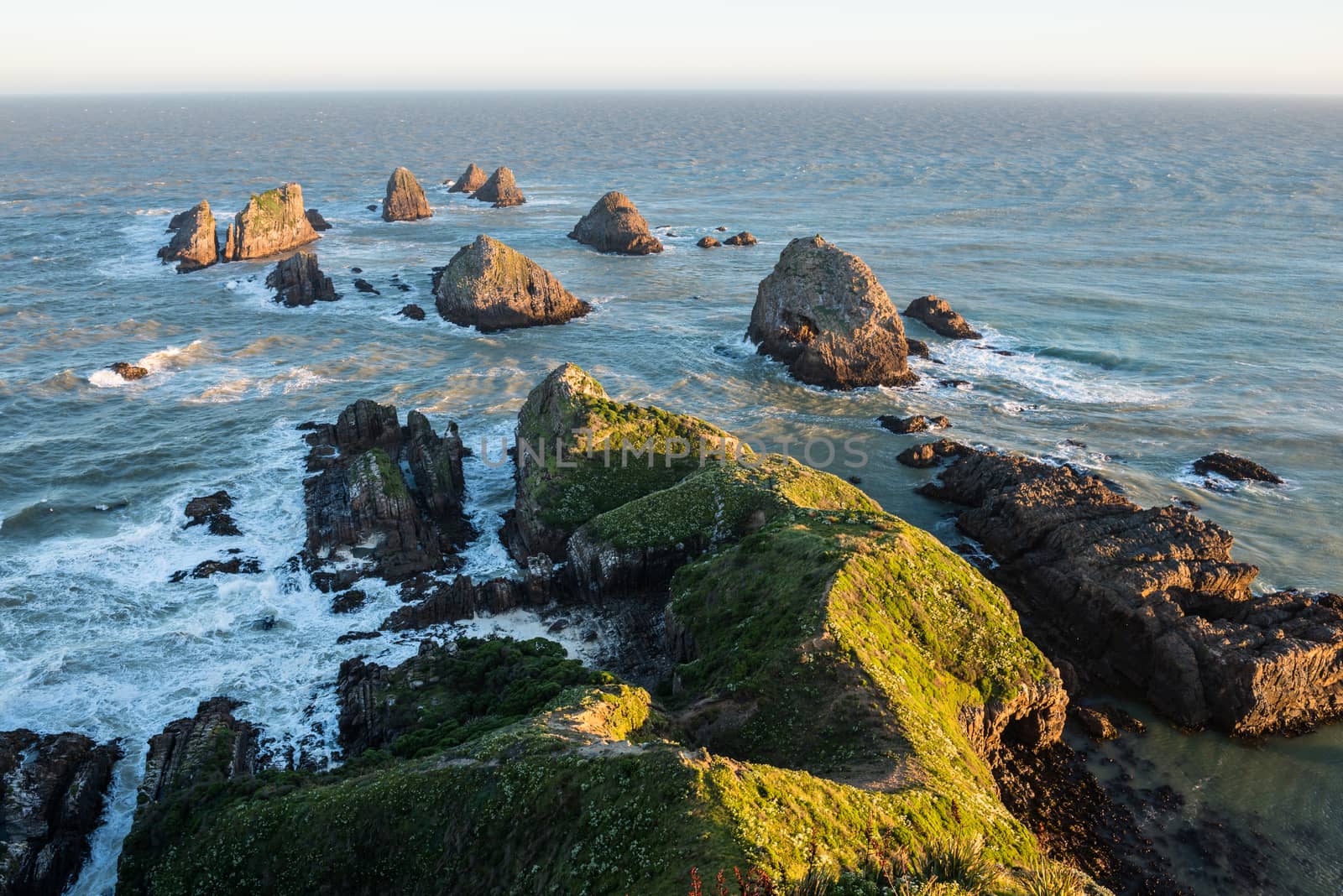 The setting sun illuminates boulders and waves of Nugget Point, the end of the New Zealand