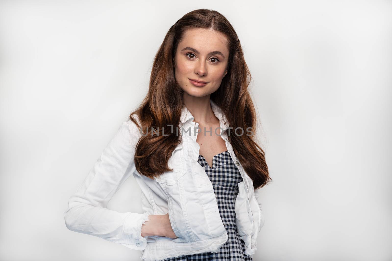Close up shot of stylish young woman in white jeans jacket smiling in front of grey background. Beautiful female model with copy space.