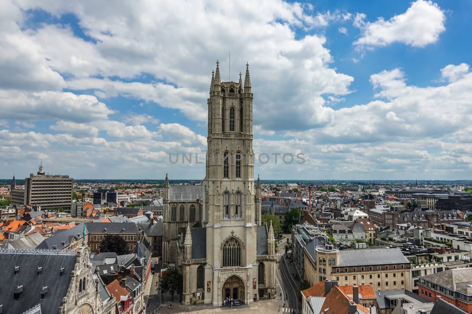 Gent, Flanders, Belgium -  June 21, 2019: Shot from top Belfry. Sint-Baafs Cathedral and closeup of tower against blue sky with cloudscape. Cityscape of roofs and buildings up to flat horizon.