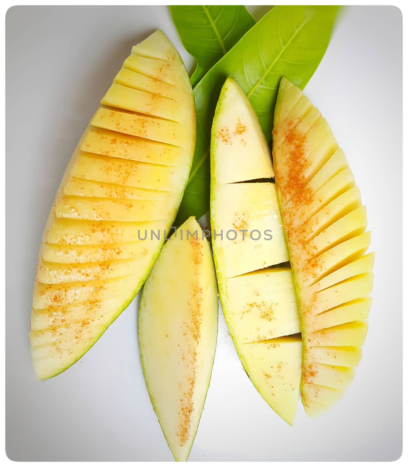 Pieces of mango cut beautifully like slant and box slices arranged in white plate with its leaf nd summer fruit and good for health also