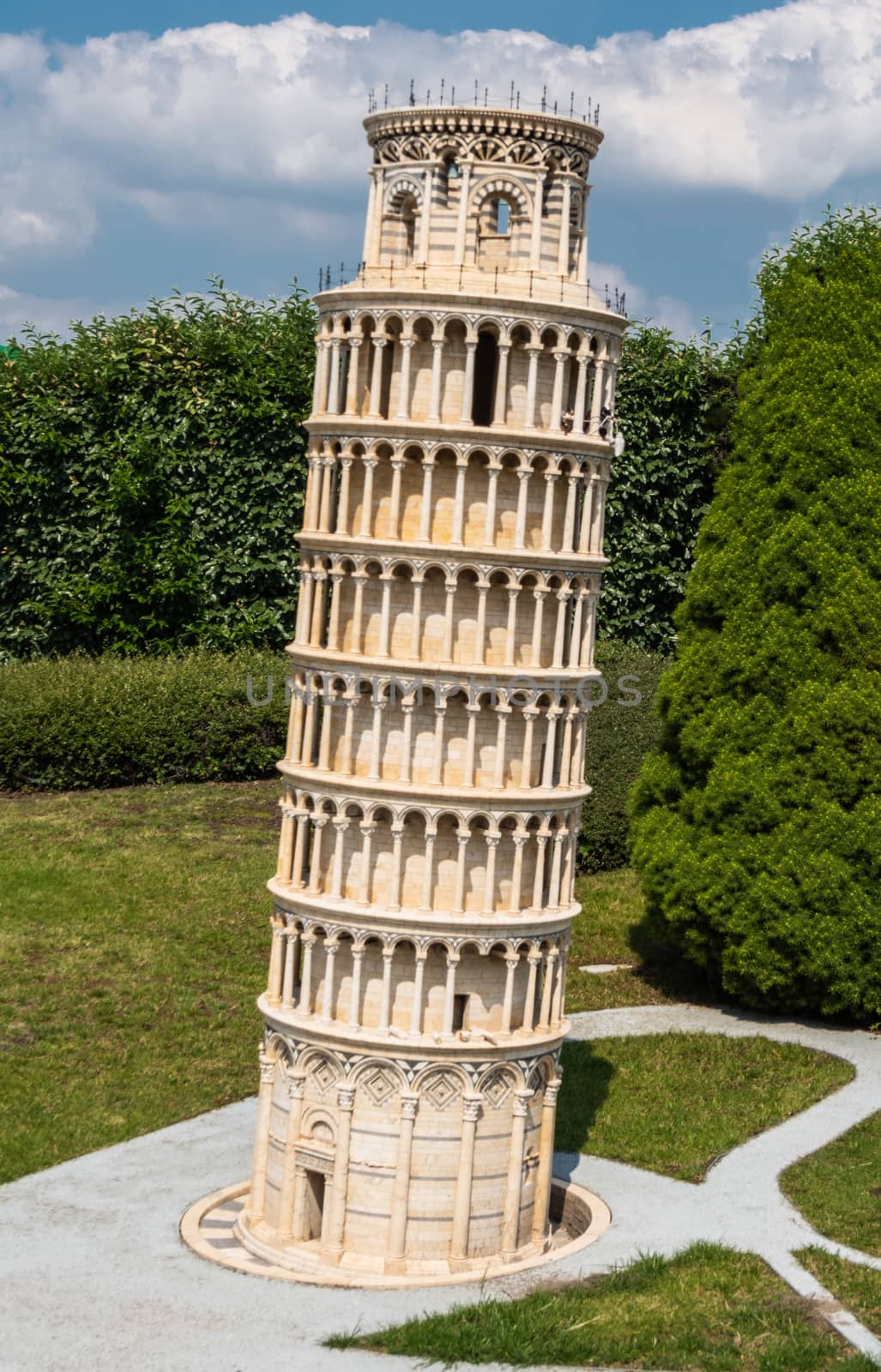 Brussels, Belgium - June 22, 2019: Mini-Europe exhibition park. Closeup of Leaning Tower of Pisa in miniature against green foliage under blue sky with white cloudscape.