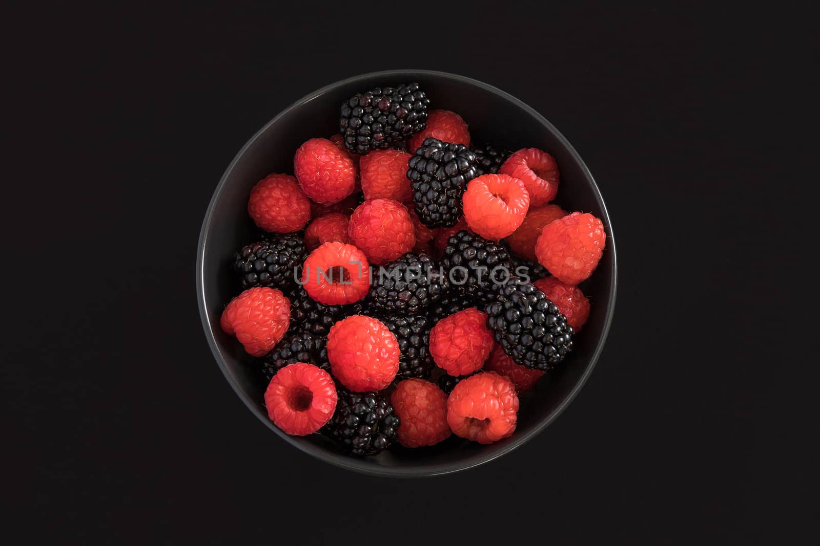 Blackberries and raspberries in a black bowl. Black background. Top view.