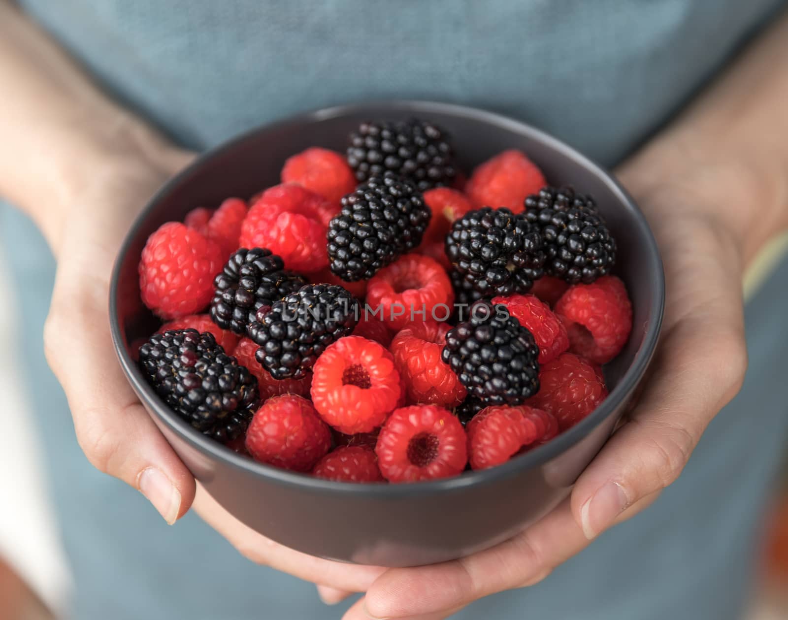 Female hands holding a bowl full of blackberries and raspberries.